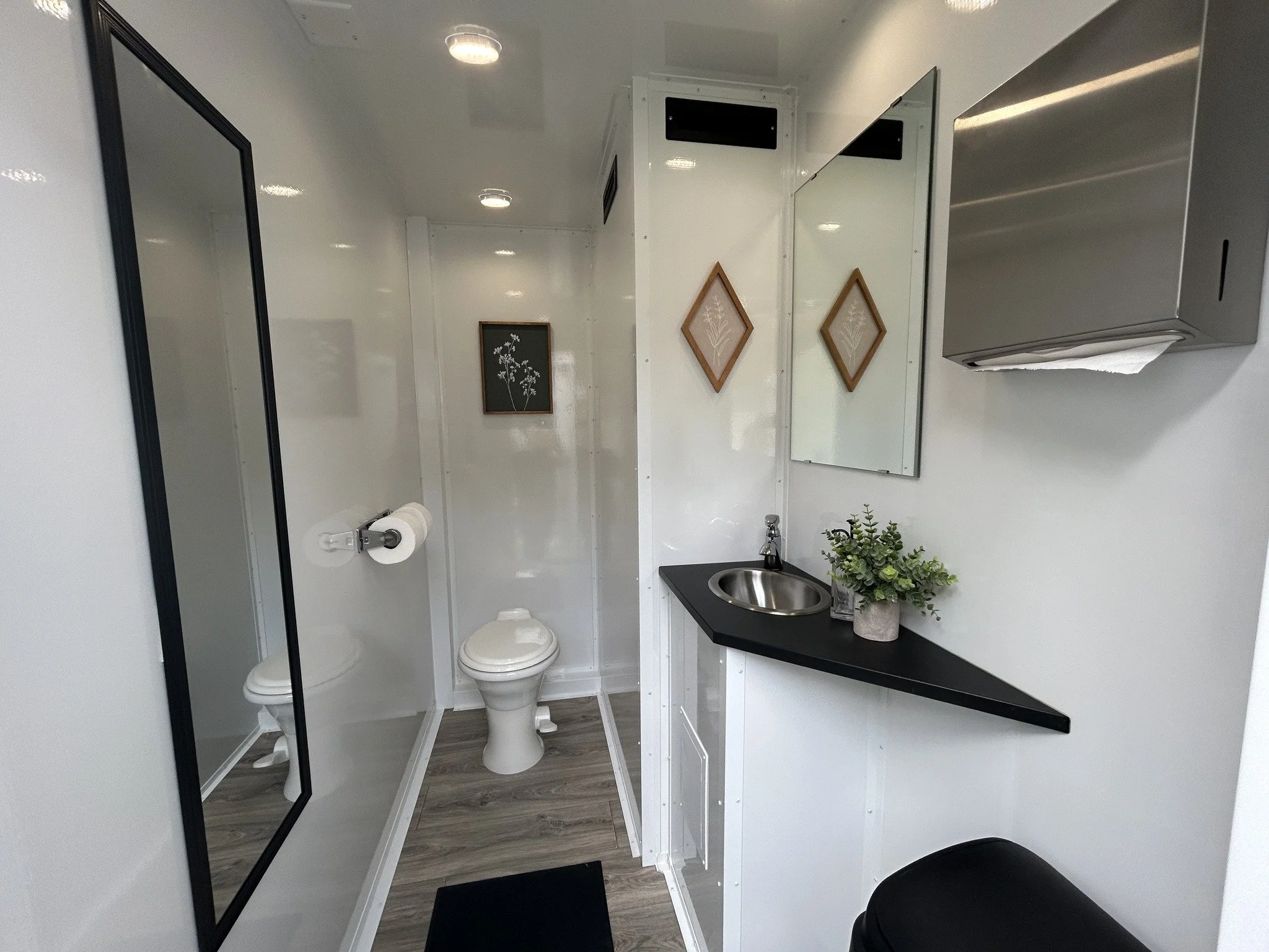 Small modern bathroom with a shower, toilet, mirror, sink, and wall-mounted paper towel dispenser.
