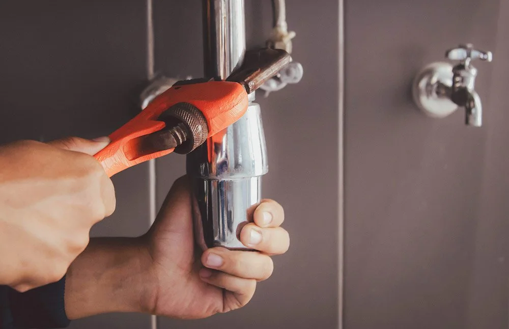 Person using a wrench to tighten or loosen a pipe connected to a water fountain or dispenser in a utility room.