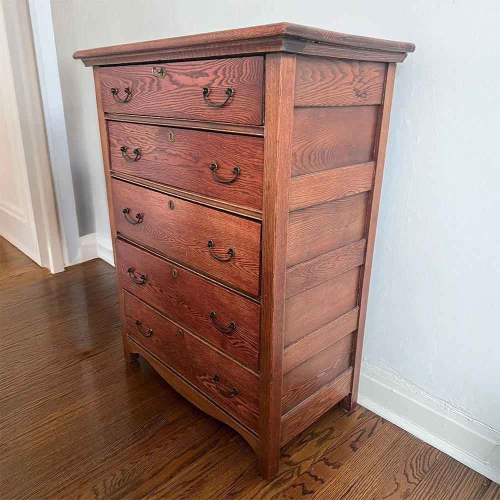 A tall wooden dresser with six drawers, each with metal handles, standing on a hardwood floor against a light-colored wall.