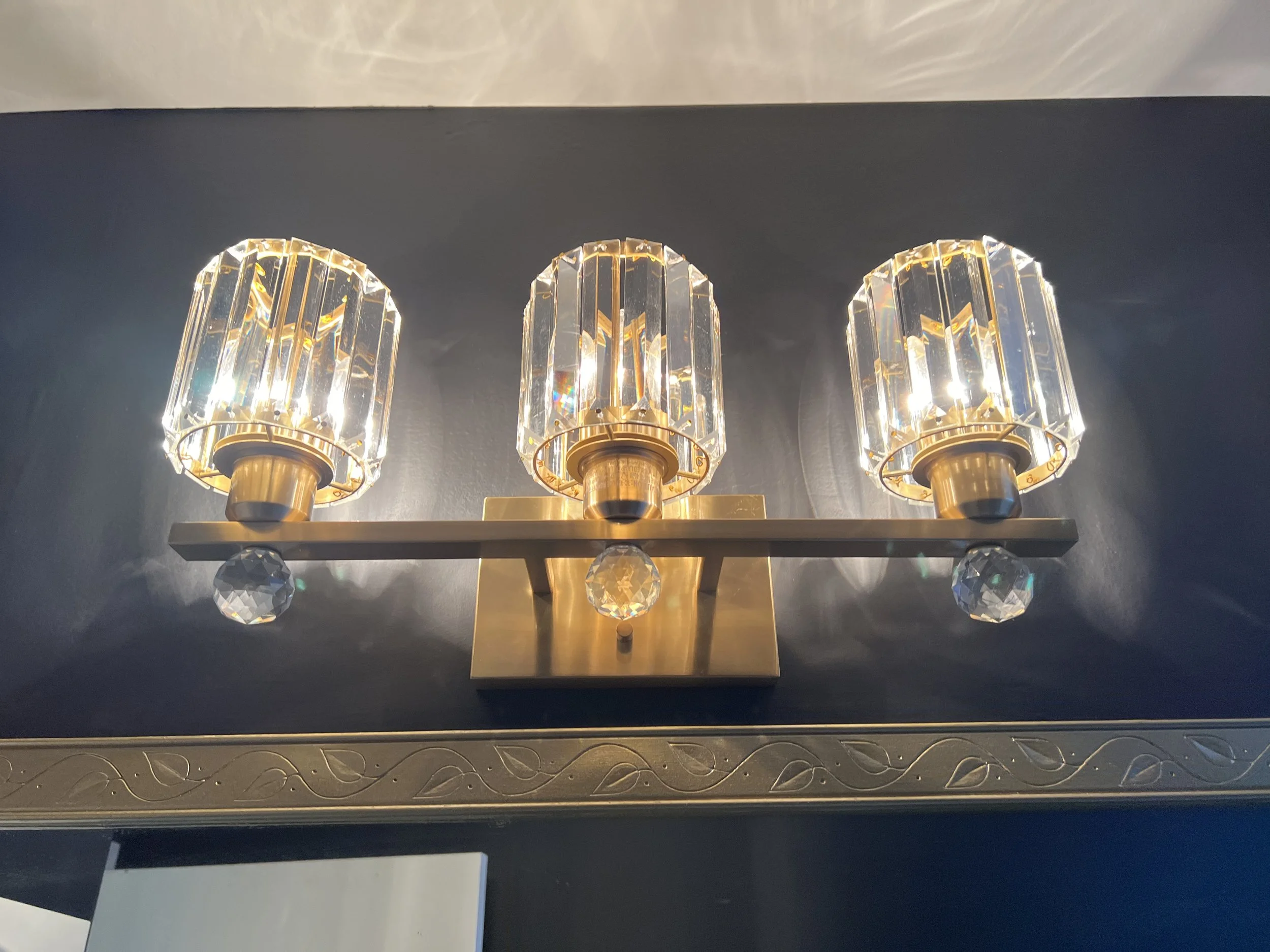 A three-light wall sconce with crystal accents on a dark wall.