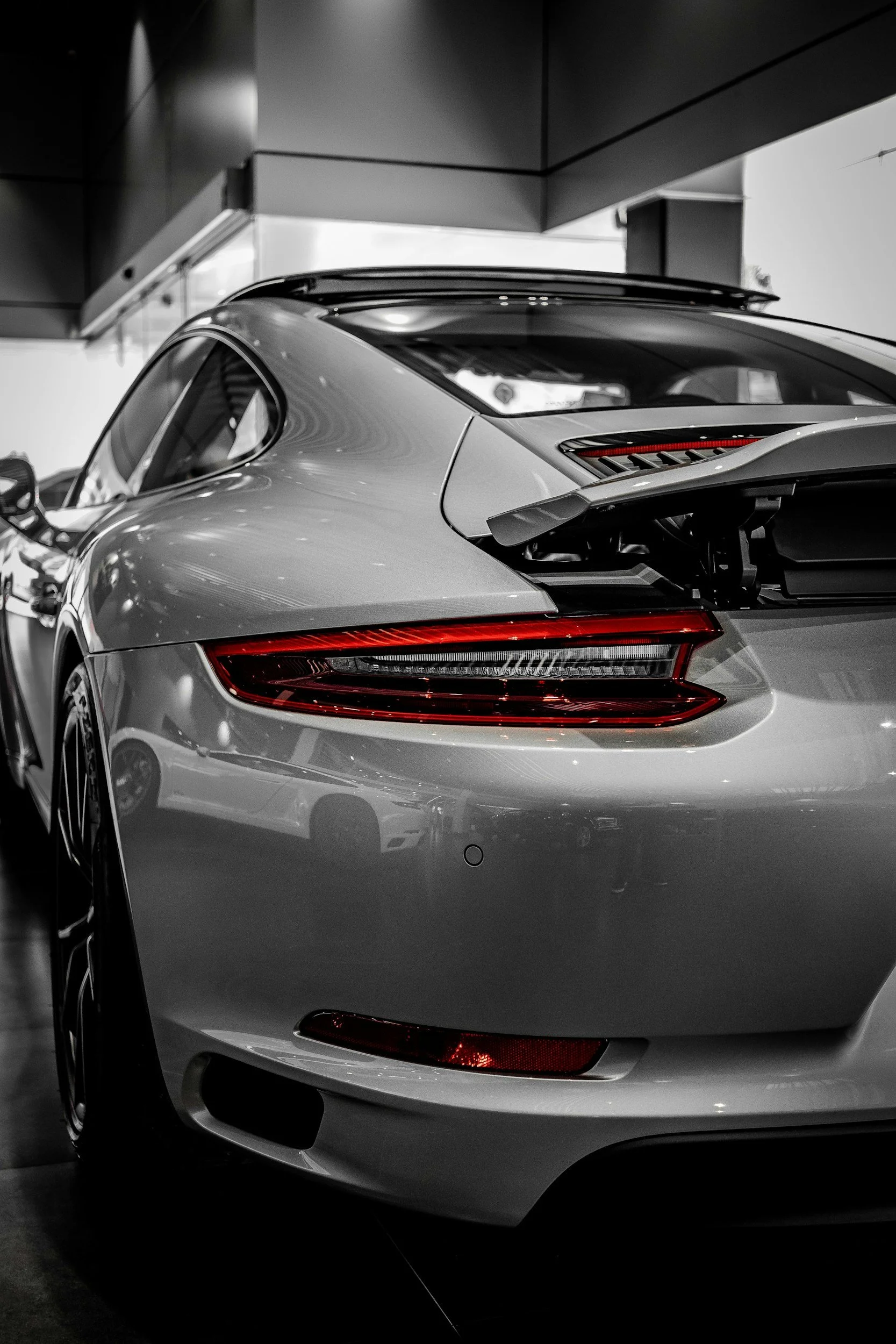 A silver luxury sports car displayed in a showroom, view of the rear and side, with a sleek design and modern lighting.