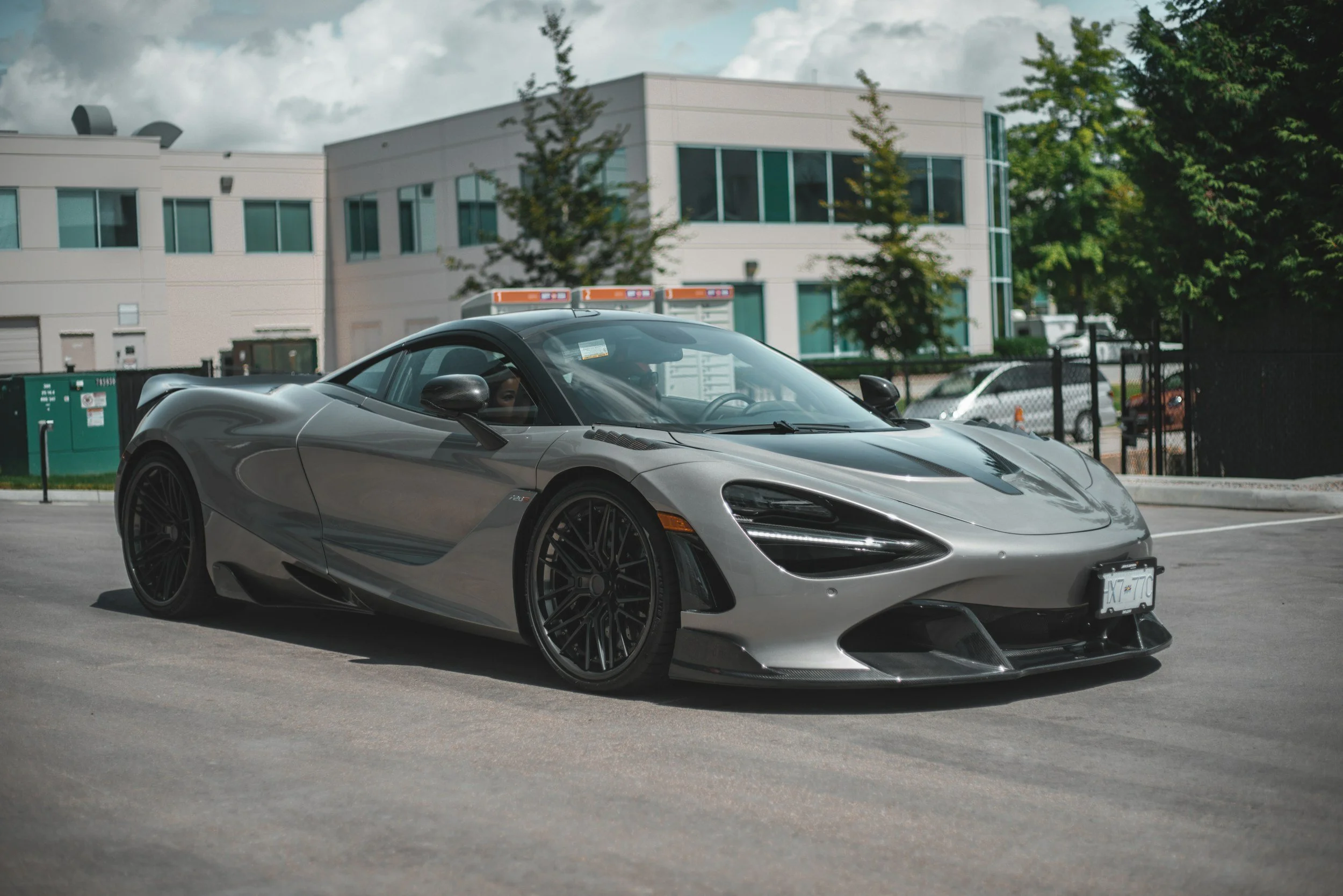 A sleek silver sports car parked on a city street with modern buildings and trees in the background.