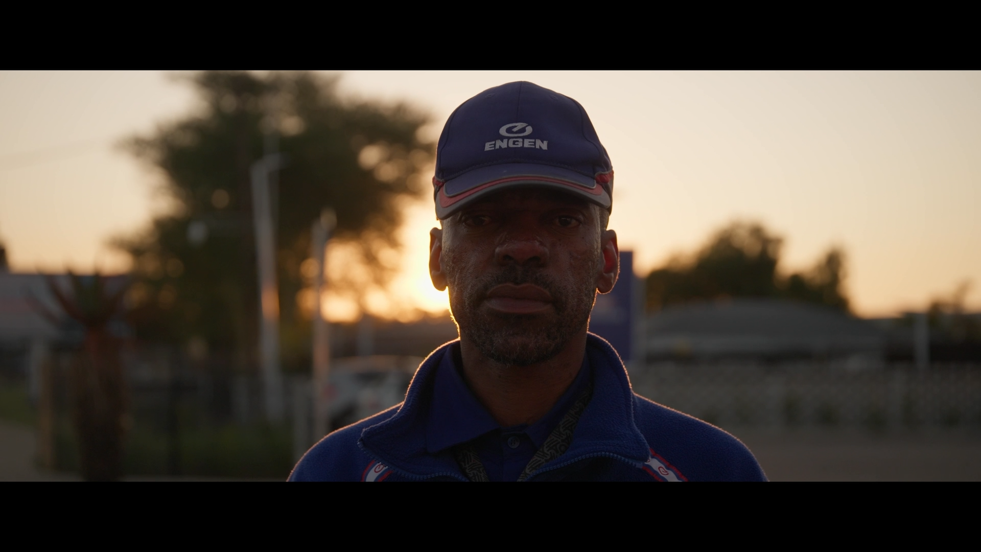 A modern house on rolling green hills with snow-capped mountains in the background under a cloudy sky.