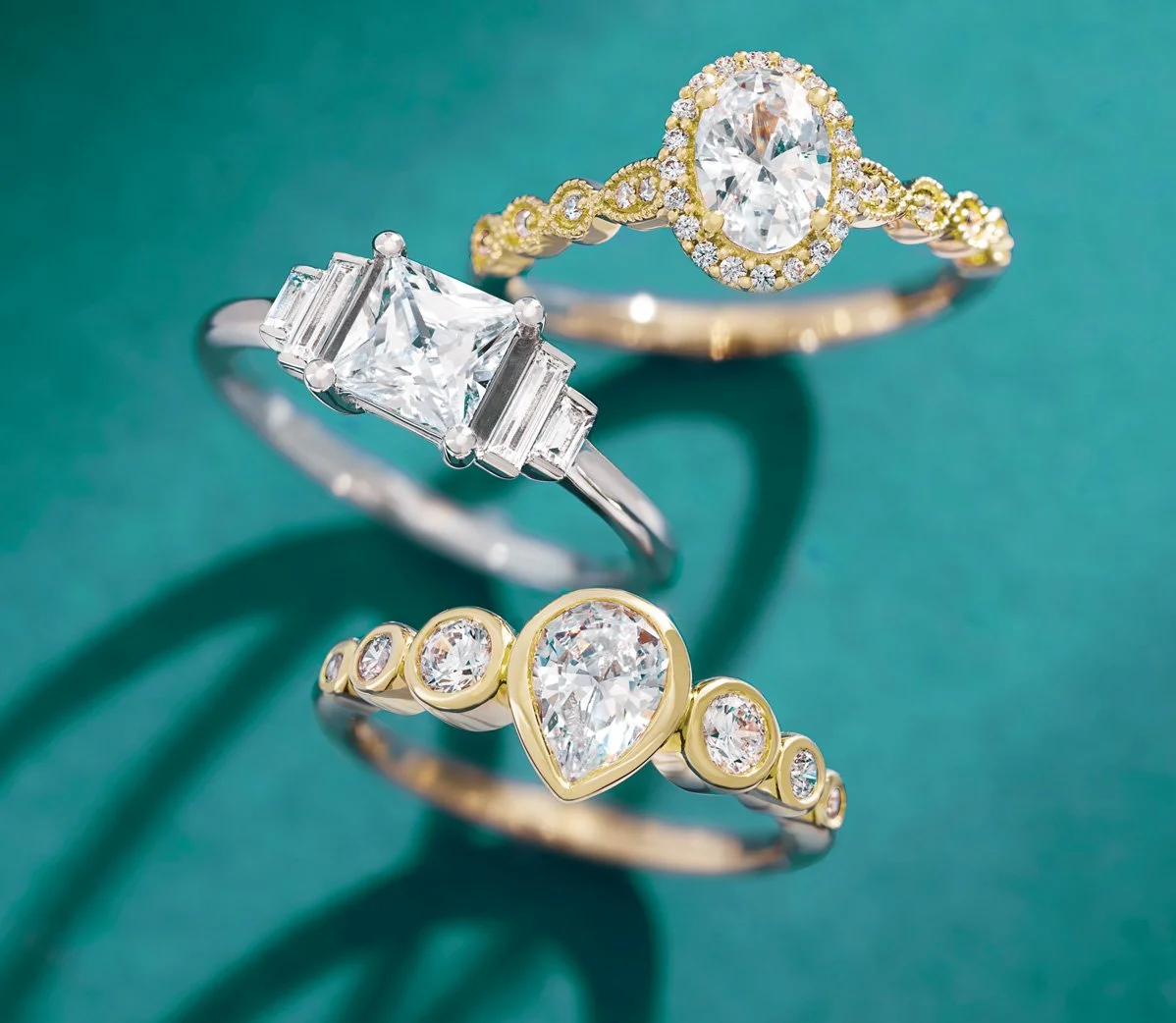 Three diamond rings with different designs on a teal background.