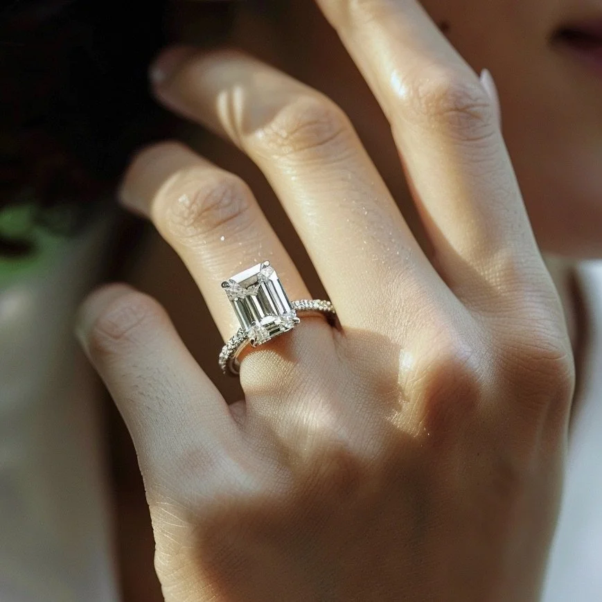 Close-up of a woman's hand wearing an emerald-cut diamond engagement ring with a diamond-studded band.