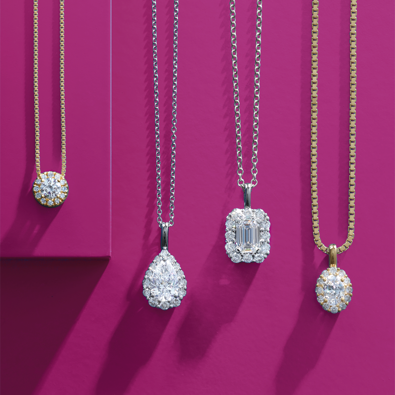 Line of five diamond pendant necklaces on pink background.