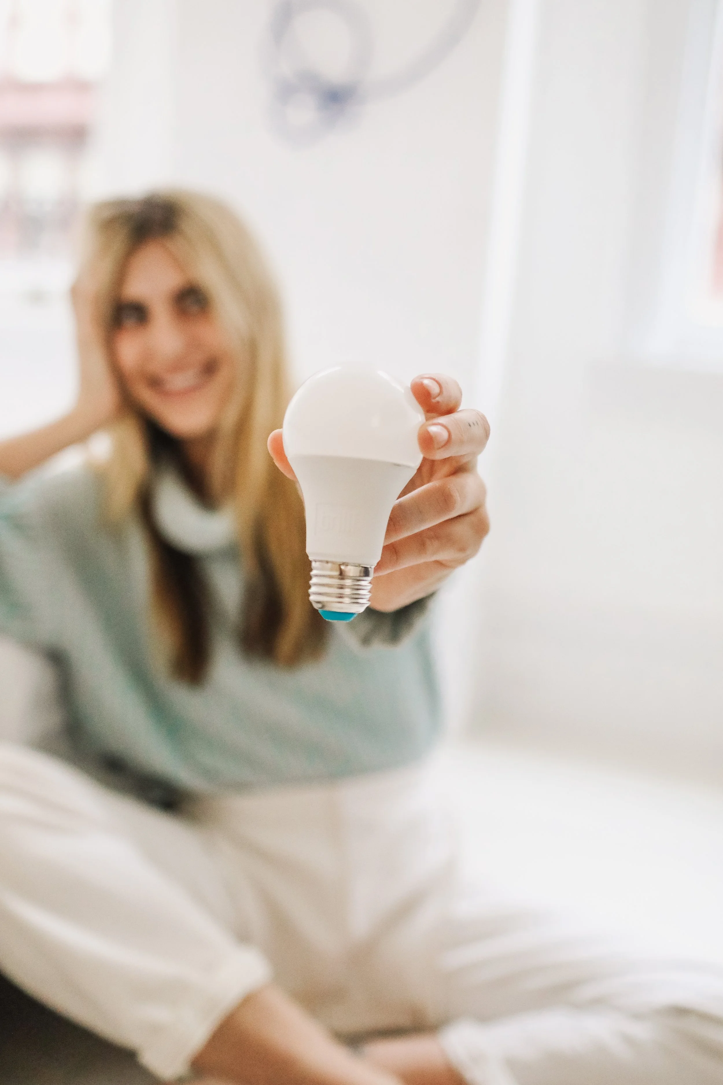 A woman holding out an LED light bulb towards the camera with a blurred background.