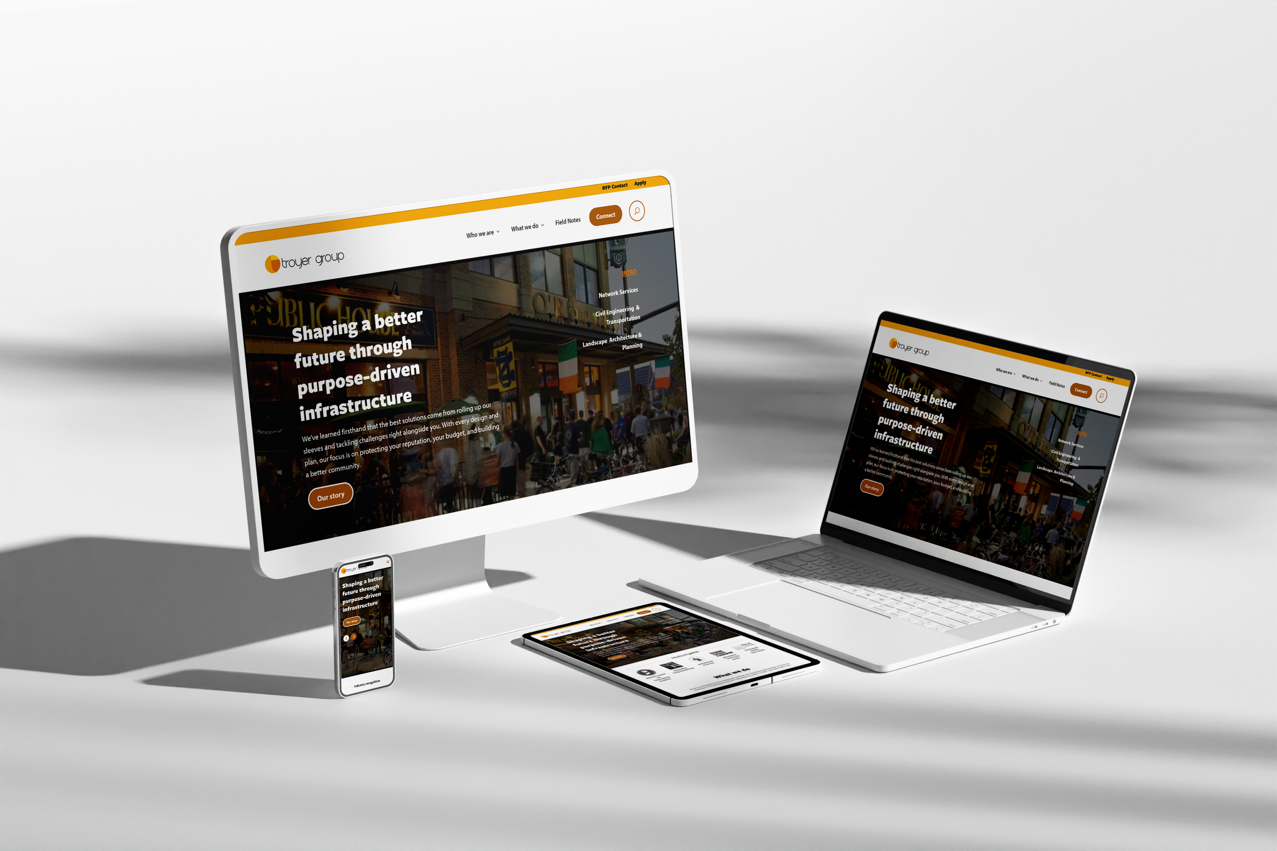 Multiple electronic devices including a smartphone, tablet, laptop, and desktop monitor displaying the same website with an orange and white theme and building images.