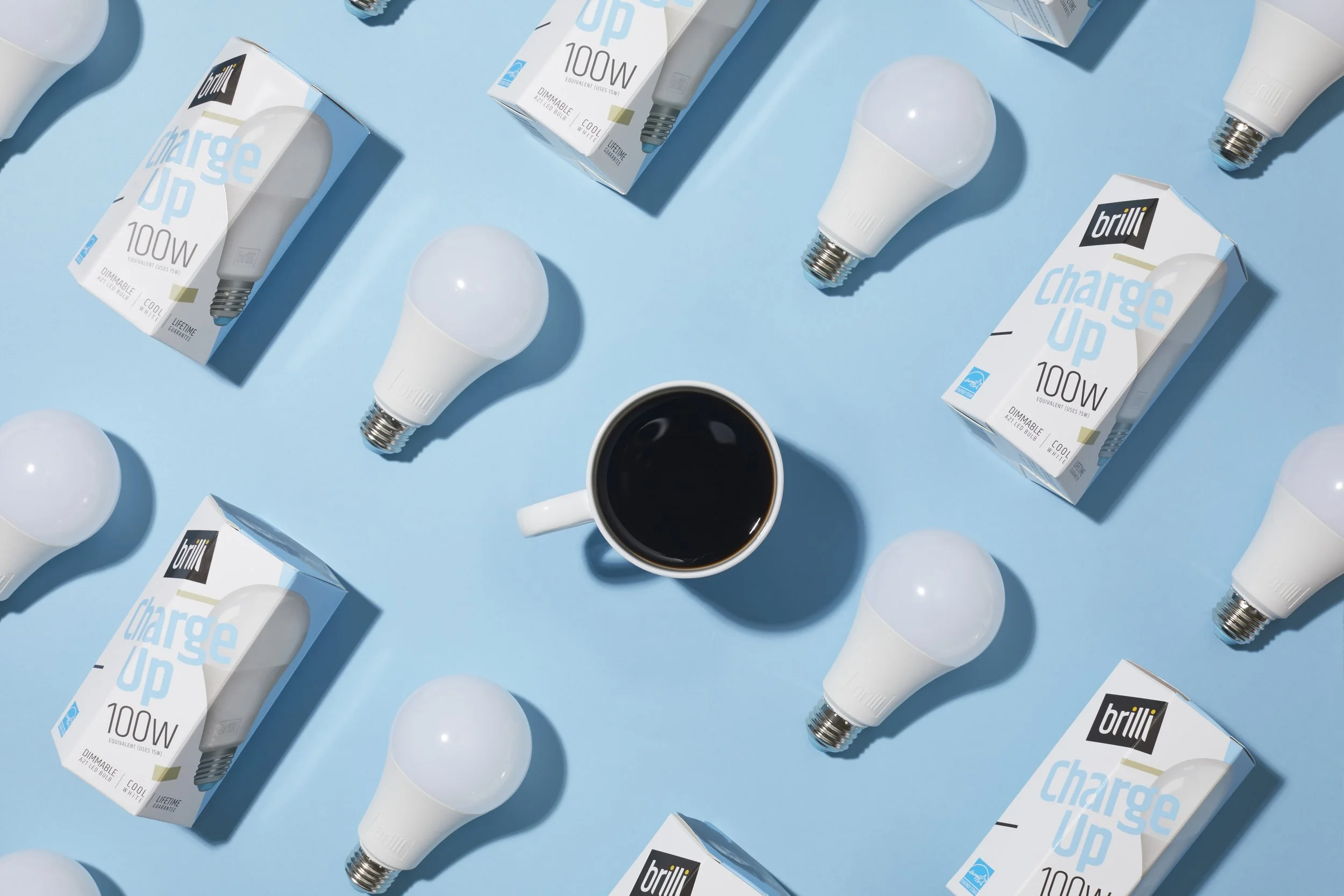 A flat lay of energy-efficient light bulbs, their boxes, and a cup of black coffee on a blue background.