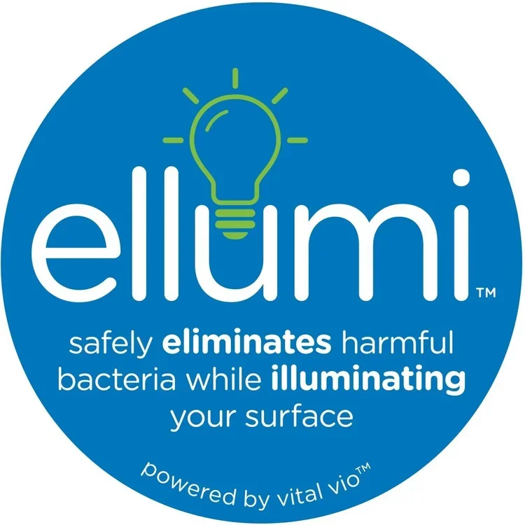 Blue circular logo with a green light bulb icon above the white text 'ellumi'. Below, it says 'safely eliminates harmful bacteria while illuminating your surface' in white text, with 'eliminates' and 'illuminating' in bold. The phrase 'powered by vital vim' is curved along the bottom edge of the circle.