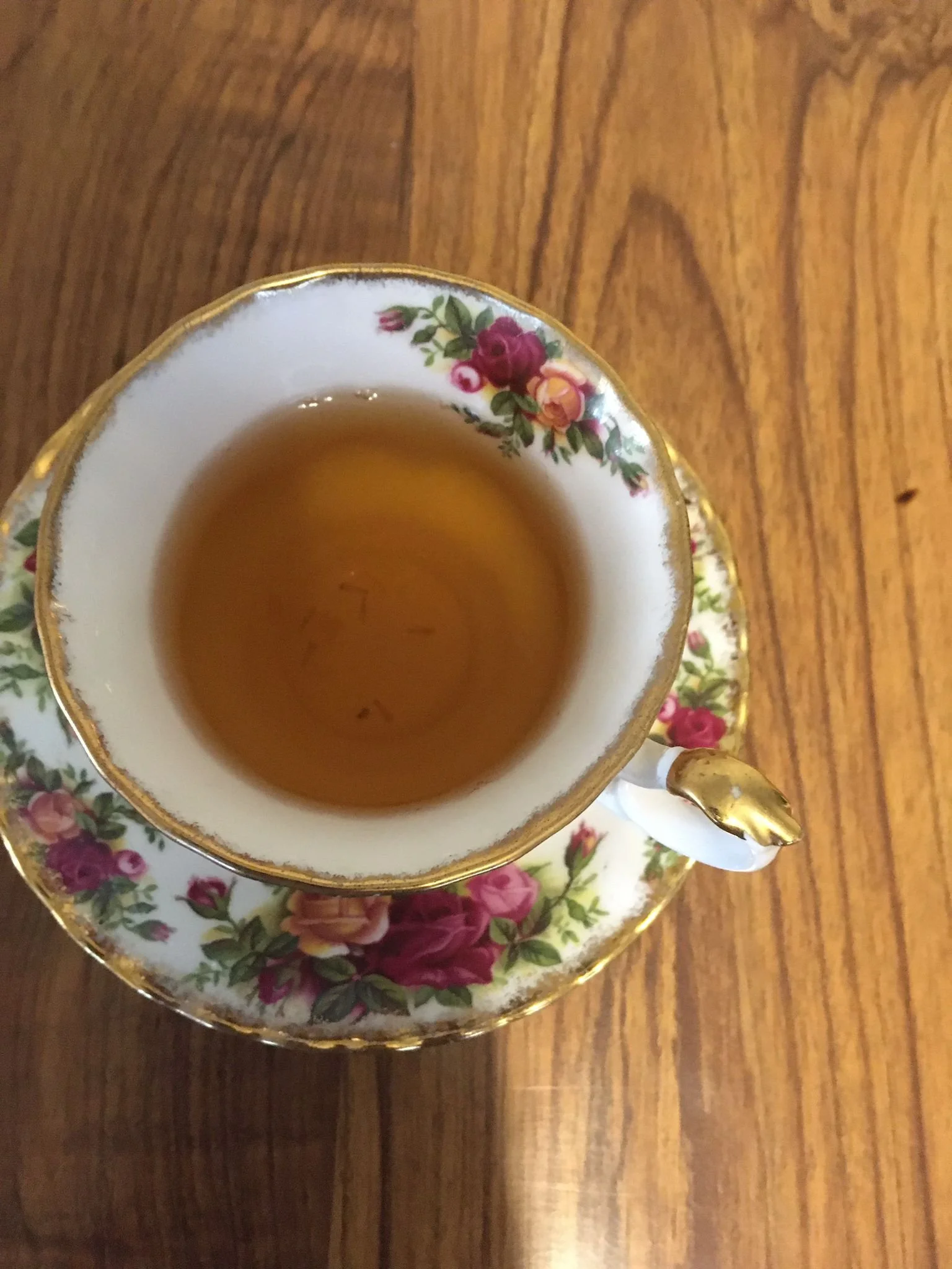 A porcelain teacup with a floral pattern and gold trim, filled with tea, sitting on a matching saucer on a wooden table.
