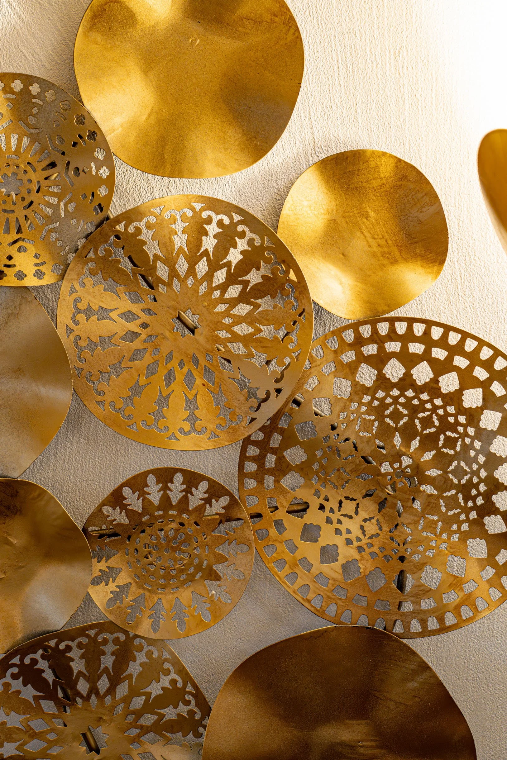 Goldene dekorative Scheiben mit verschiedenen Mustern liegen auf einer weißen Wand.