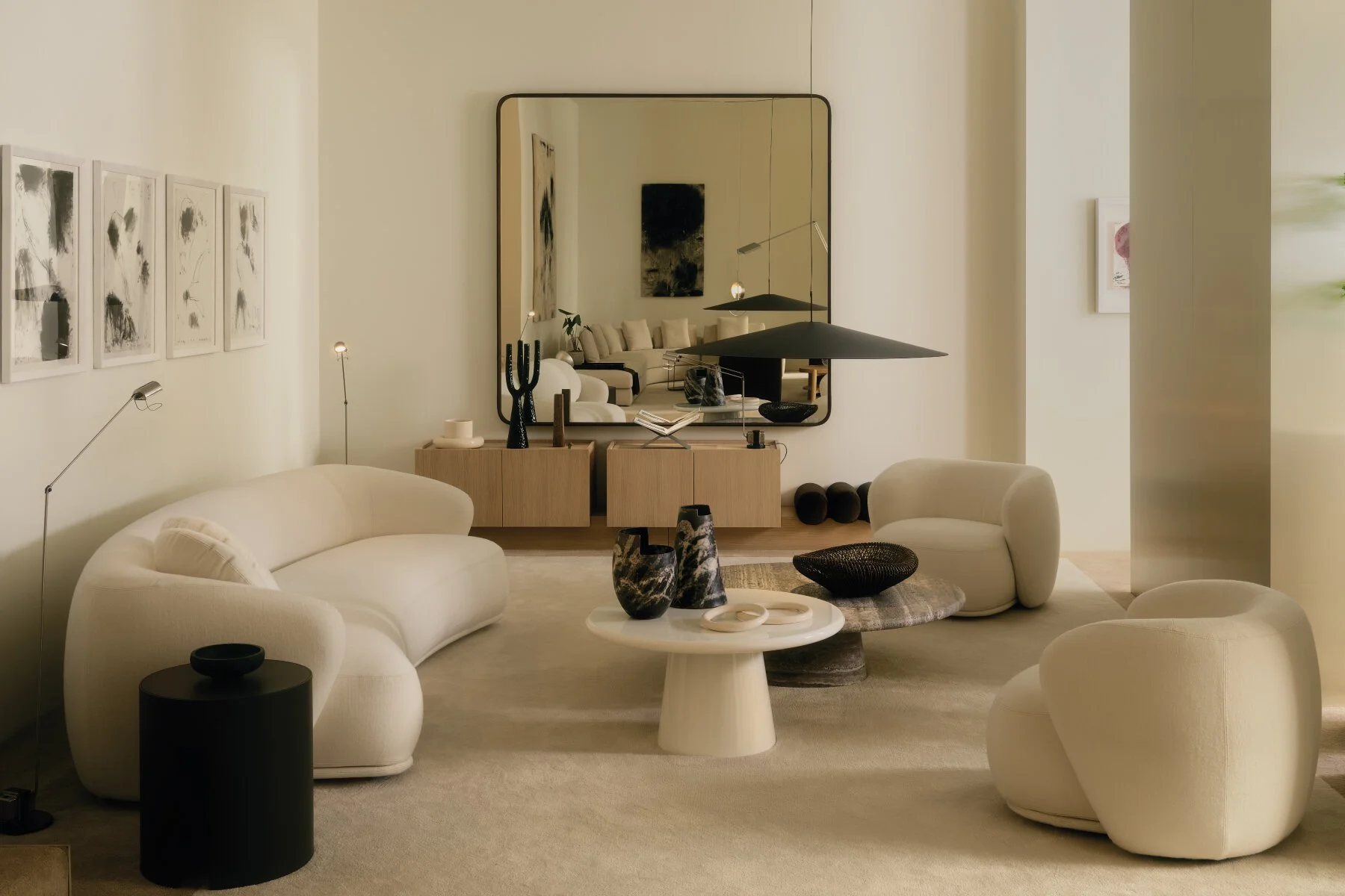 Moderner, minimalistischer Wohnraum mit weißen Sofas, abstrakten Kunstwerken, dekorativen Vasen, einem großen Spiegel und dunklen Lampen.