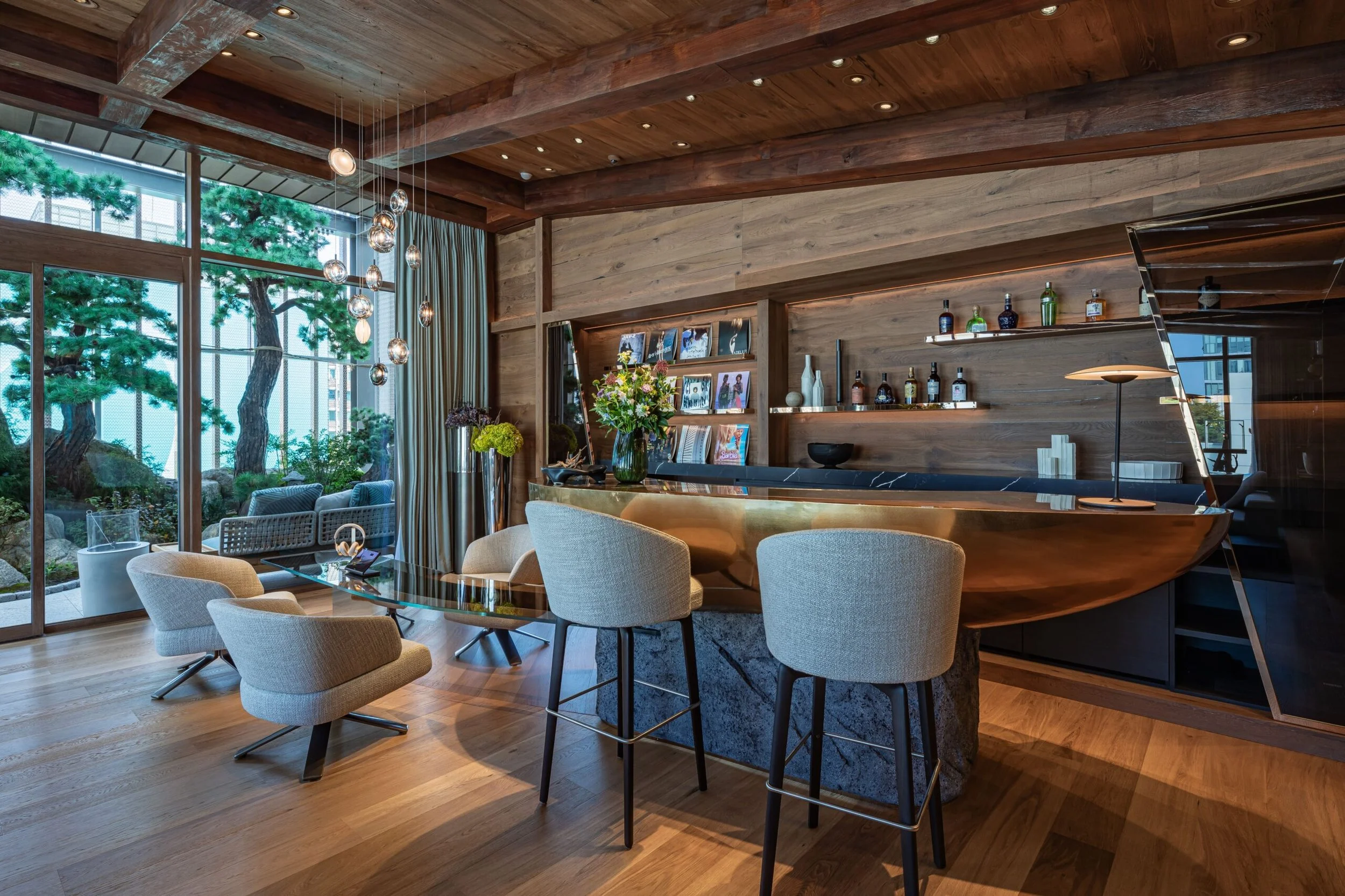 Innenaufnahme eines modernen Wohnzimmers mit Holzdecke, großen Fenstern, Pflanzen, einem weichen Sitzsessel, einem runden Tisch und einer Bar mit Spirituosen. Natürliche Lichtverhältnisse, stilvolle Dekorationen.