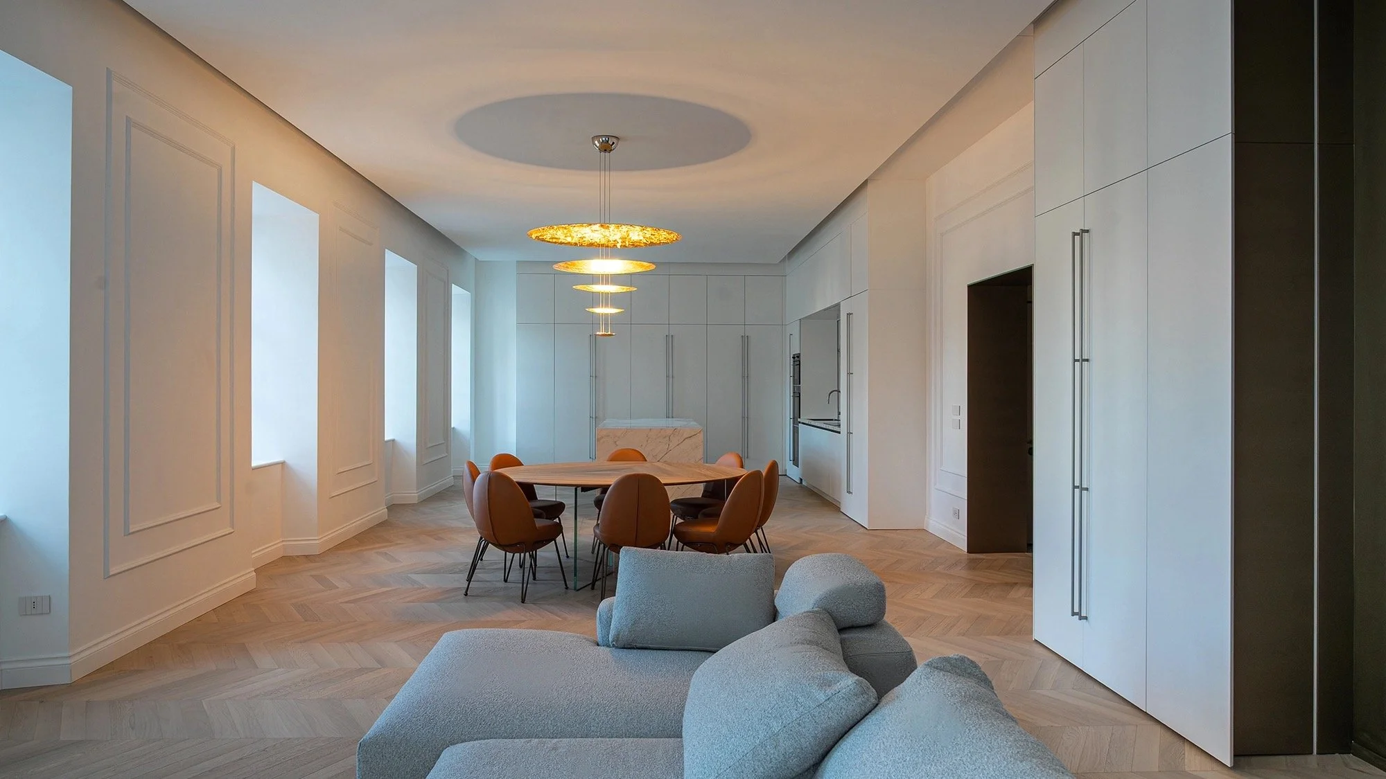 Moderne, offene Küche mit weißen Schränken, Essbereich mit runder Tisch und braunen Stühlen, Designer-Deckenleuchte, große Fenster, elegantes Interieur, Holzfußboden.