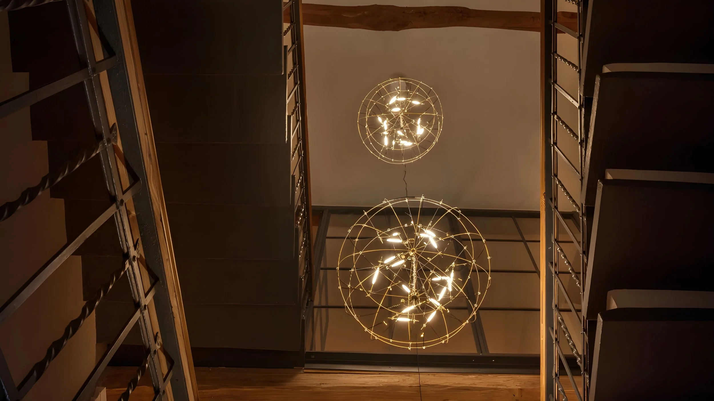 Ansicht einer modernen Innenraumgestaltung mit zwei golden leuchtenden Kugellampen, umgeben von dunklen schwarzen Wänden und Holzdetails, gesehen von unten.