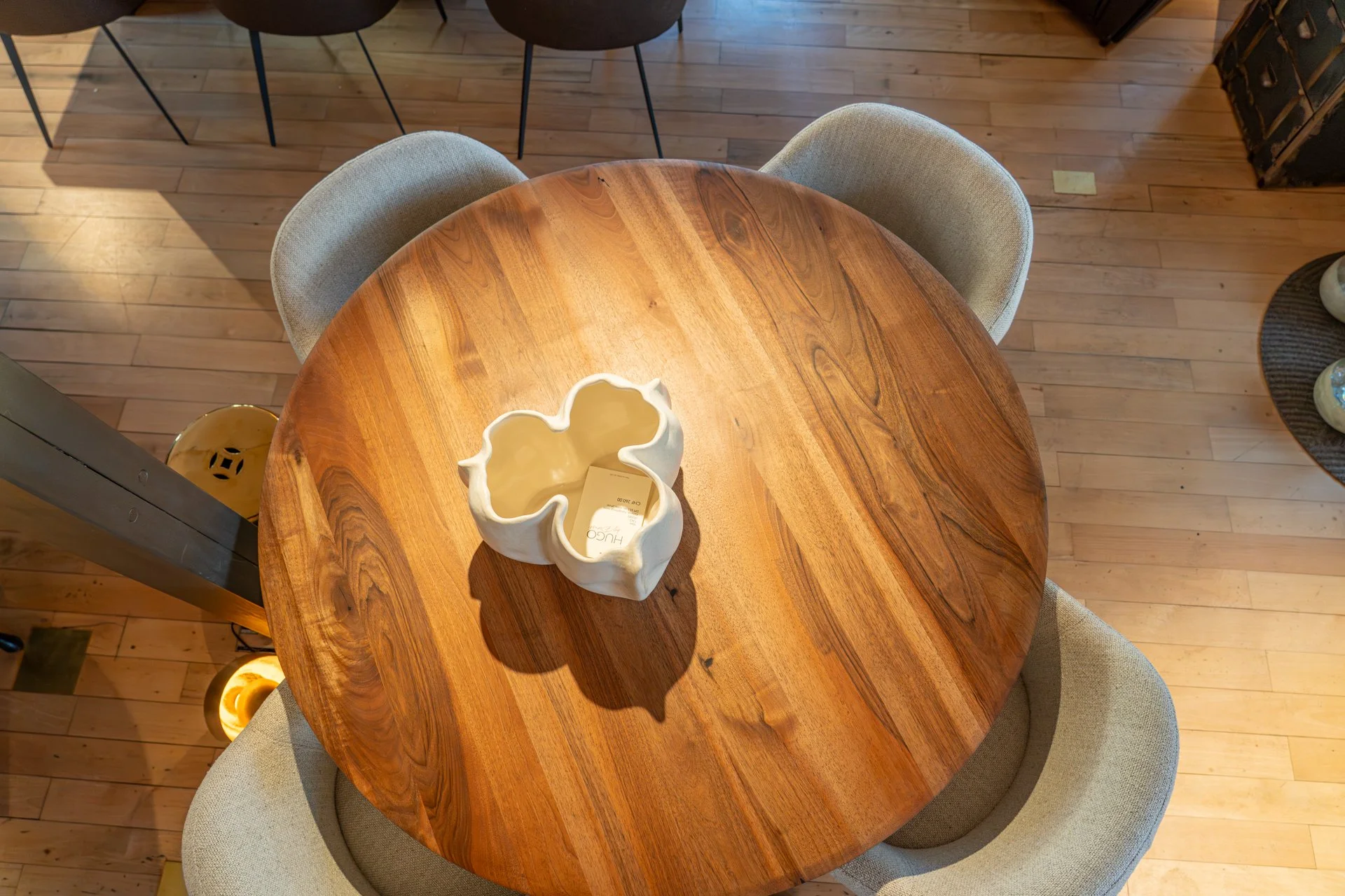 Runder Holztisch mit einer weißen Blumenvase in der Mitte, eingerahmt von zwei beigen Stühlen, im Raum mit Holzfußboden.