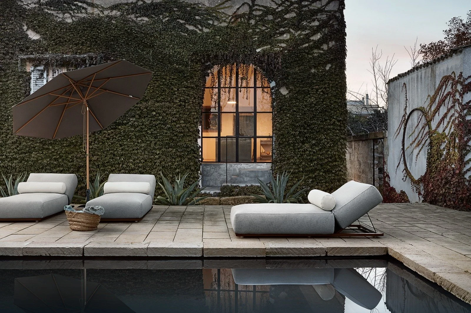 Garten mit Liegestühlen, Sonnenschirm und einem Pool bei Sonnenuntergang, umgeben von vertikaler Begrünung und einer alten Fassade.