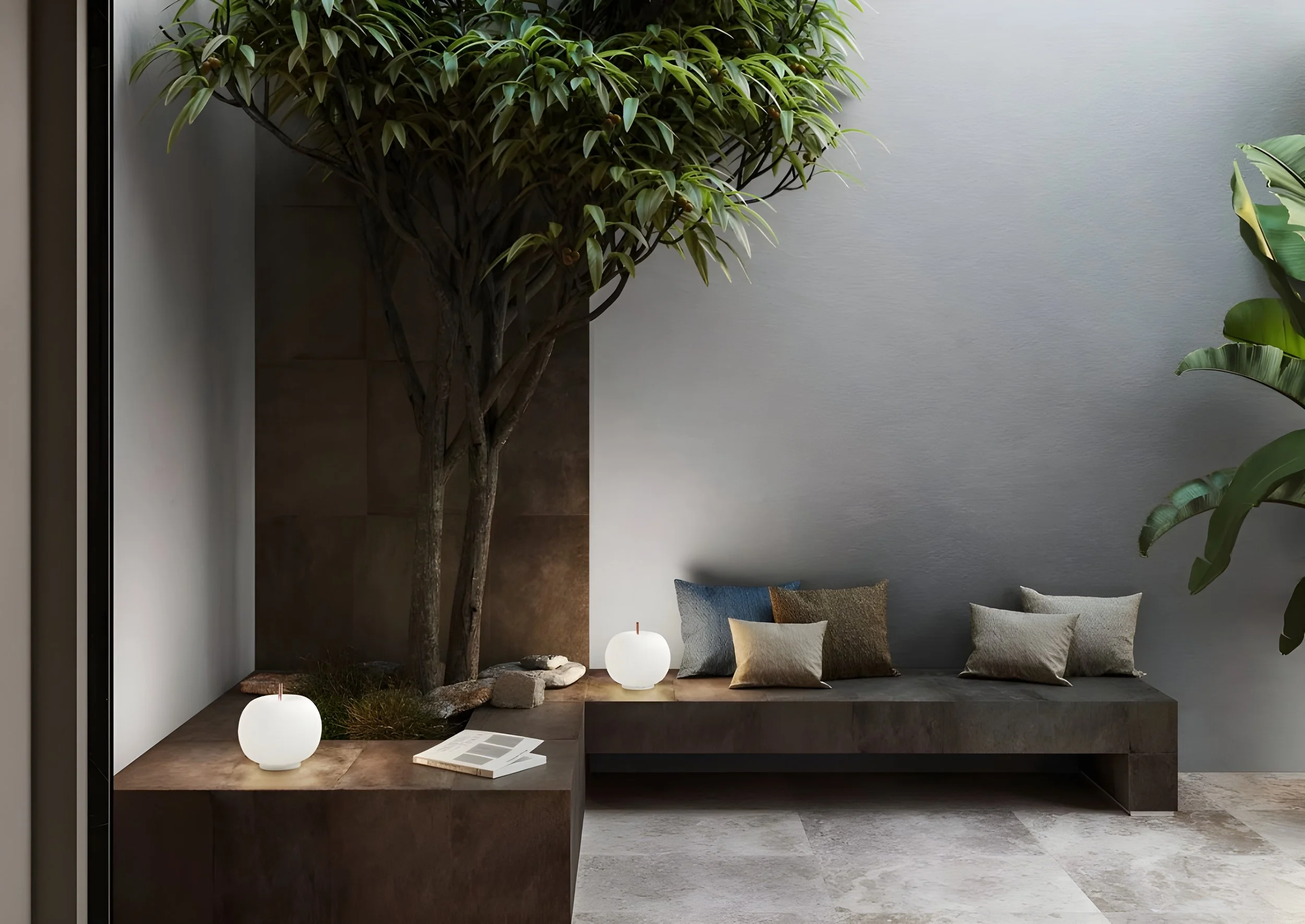 Ein modernes Wohnzimmer mit einem großen Baum in der Ecke, Kerzen auf dem Boden, Kissen auf einer Bank und Blätterpflanzen an der Wand.