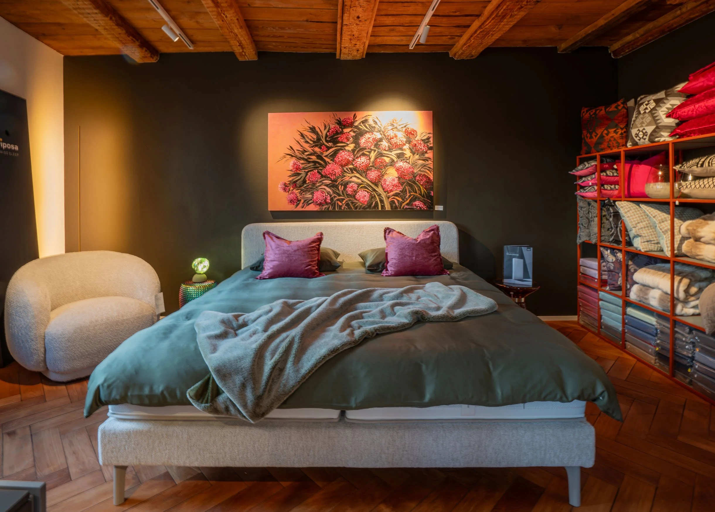 Ein Schlafzimmer mit einem Himmelbett, bunten Kissen, Wandbild und einer roten Regalwand mit Kleidung und Dekoration.