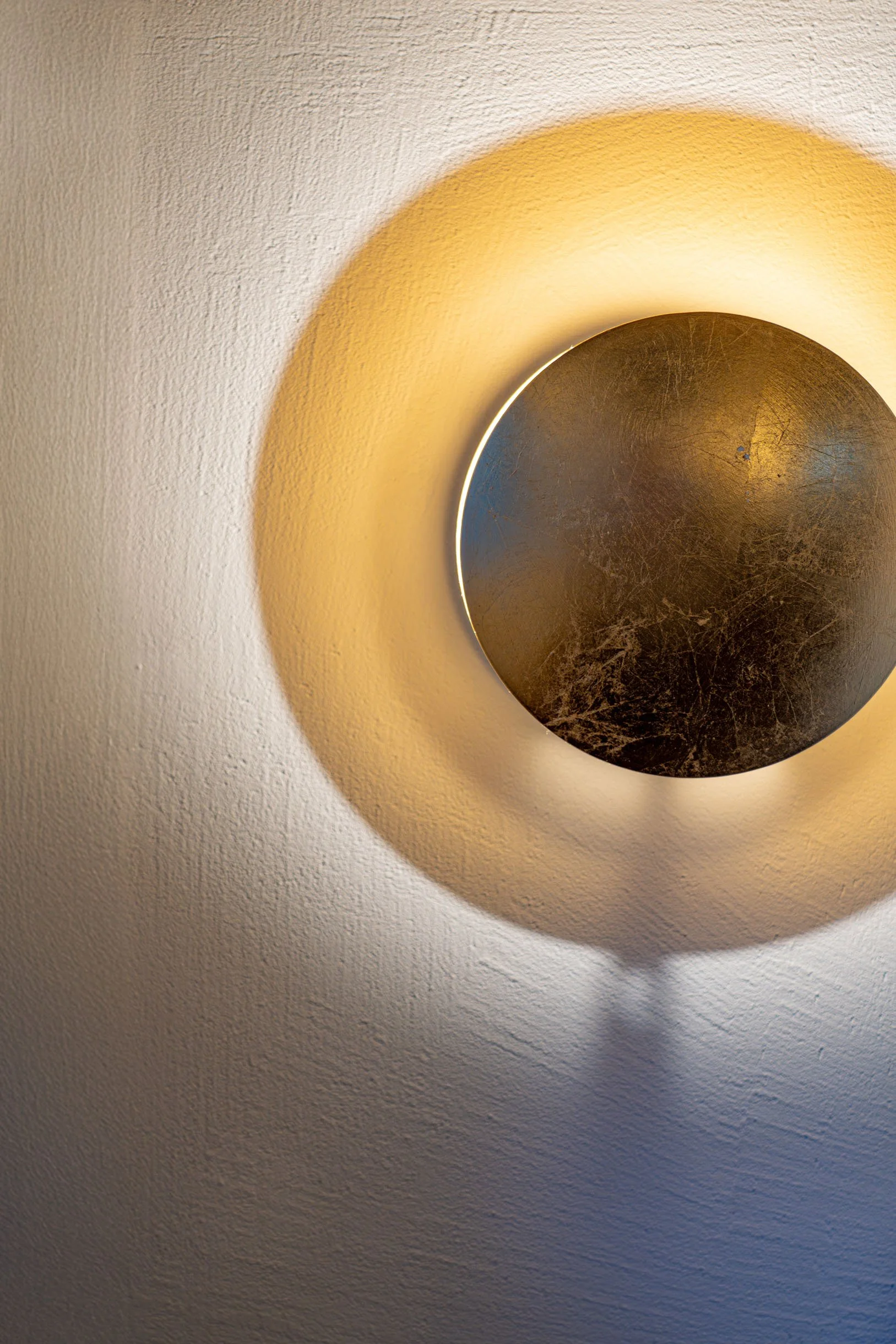 Runde Metallwandlampe, die einen warmen Lichteffekt an die weiße Wand wirft.