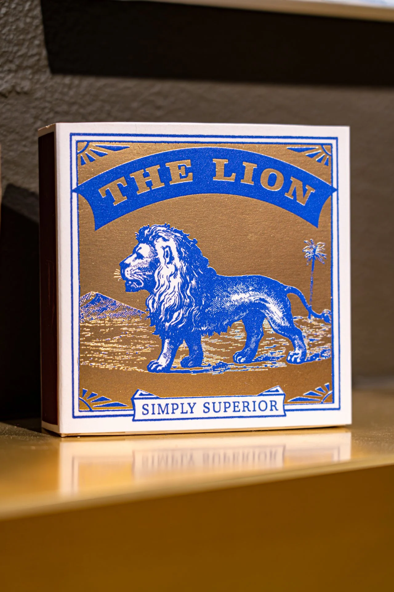 Eine Schachtel mit blauer und goldener Aufmachung, auf der ein Löwe abgebildet ist, mit dem Text "The Lion" und dem Slogan "Simply Superior".