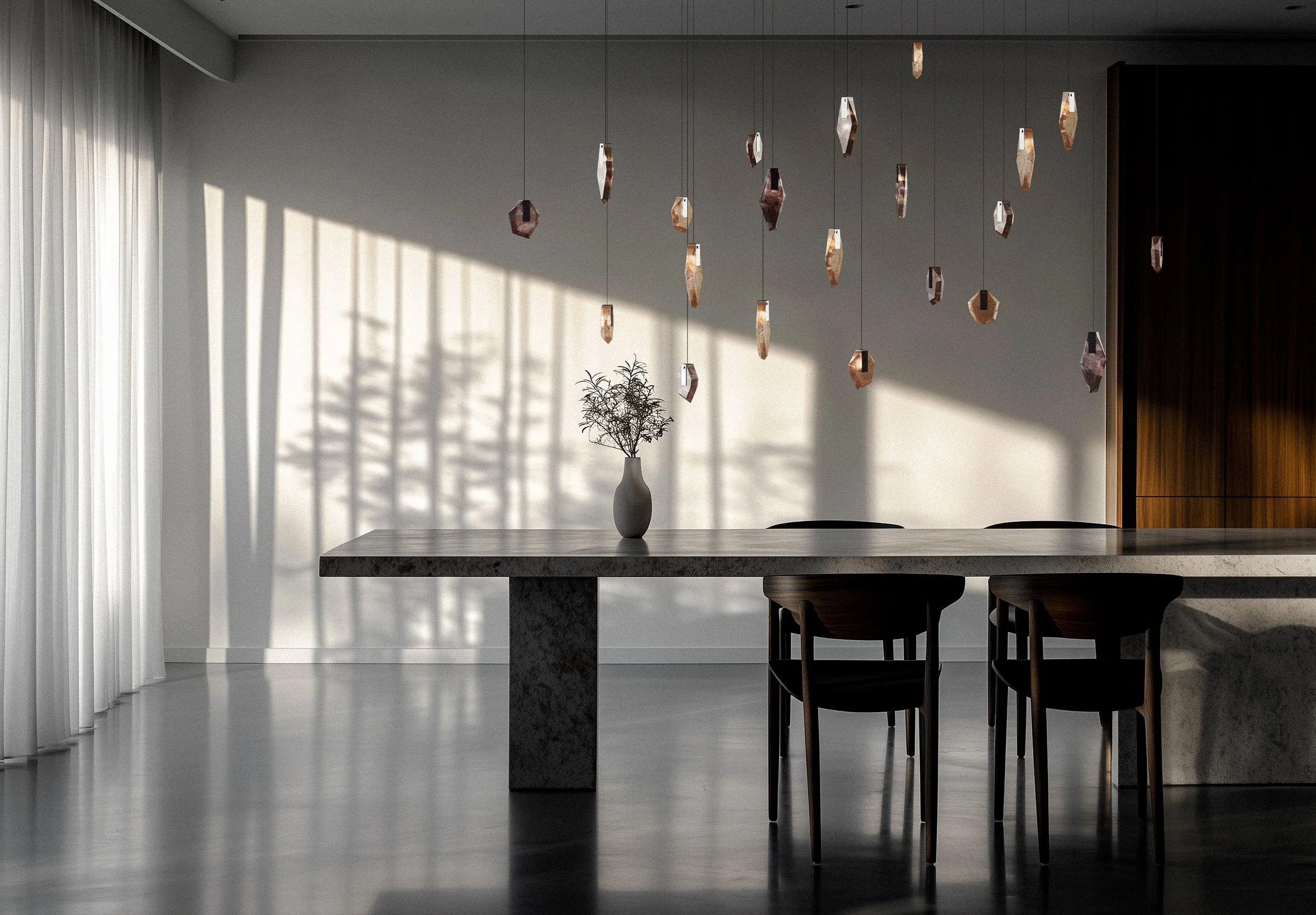 Ein moderner Essbereich mit einem grauen Marmortisch, schwarzen Stühlen und einer weißen Vase mit einer Pflanze. Hängende Lampen aus Kupfer hängen von der Decke. Natürlicher Lichteinfall schafft Schatten an der Wand.