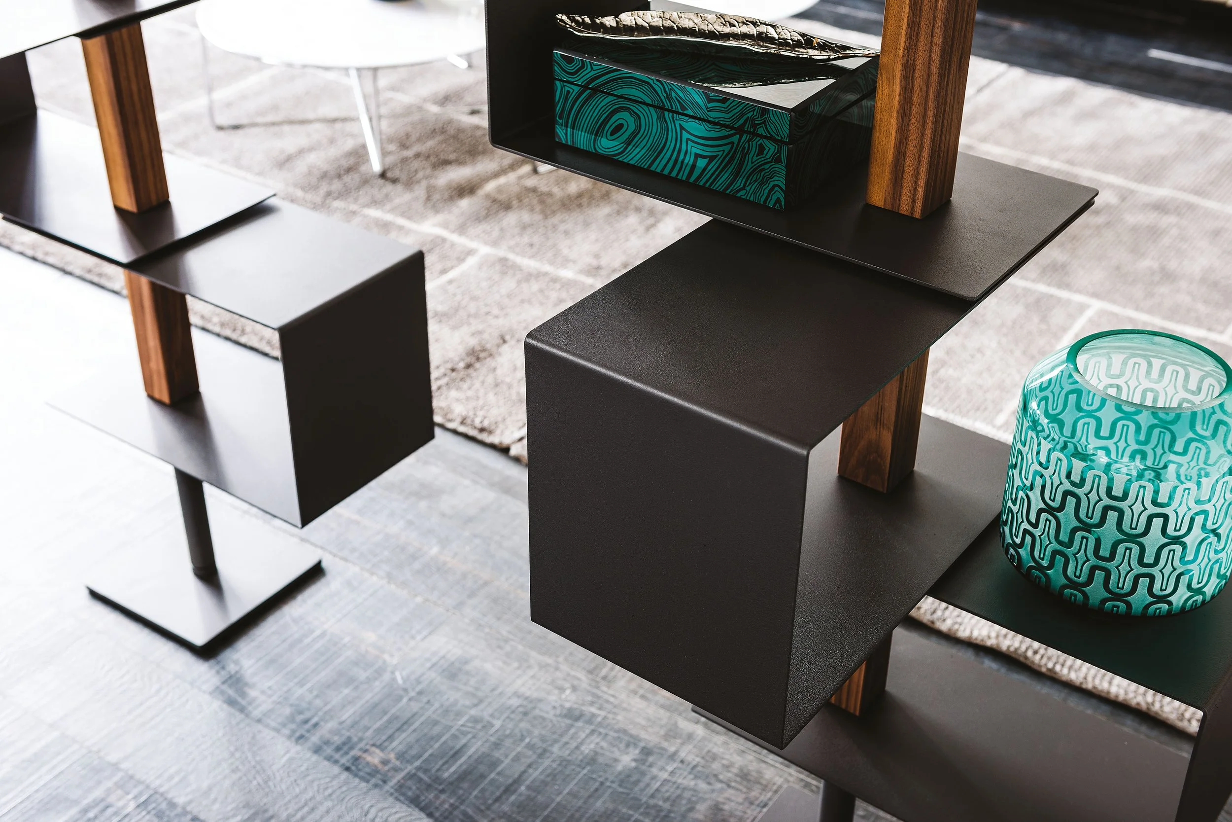 Modernes Möbelstück mit schwarzen und holzfarbenen Elementen, dekoriert mit einer blauen Vase. Der Boden ist mit einem hellen Teppich auf dunklem Holz ausgelegt.