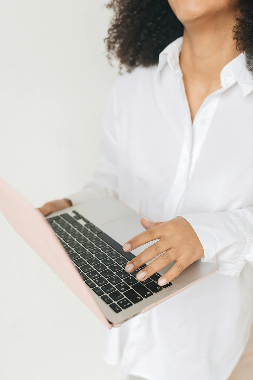 Person in a white shirt using a laptop computer with a pink case.