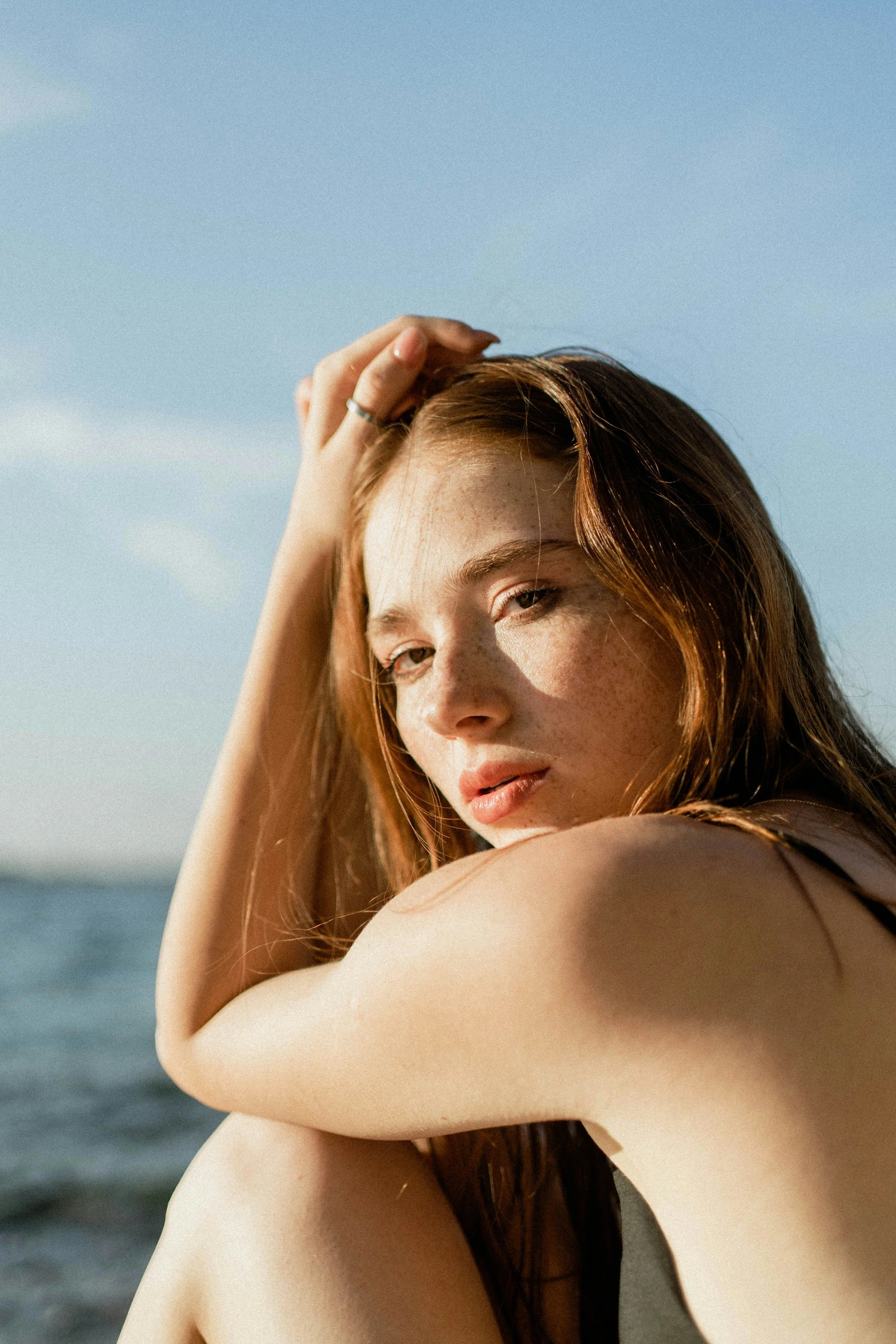 Young woman with red hair and freckles leaning on her arms near the water on a sunny day.