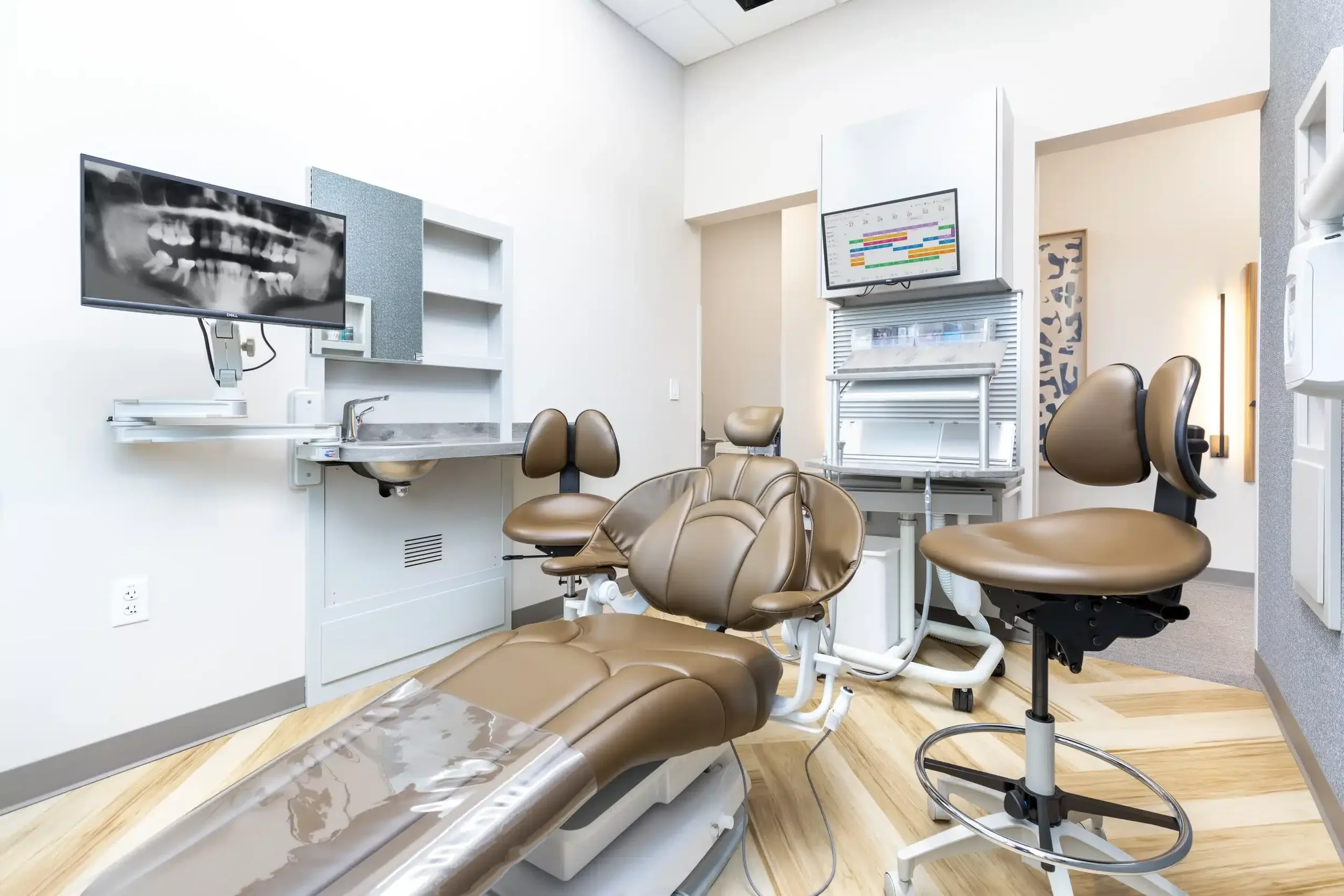 Dental examination room with dental chair, monitor displaying X-ray image, and medical equipment.