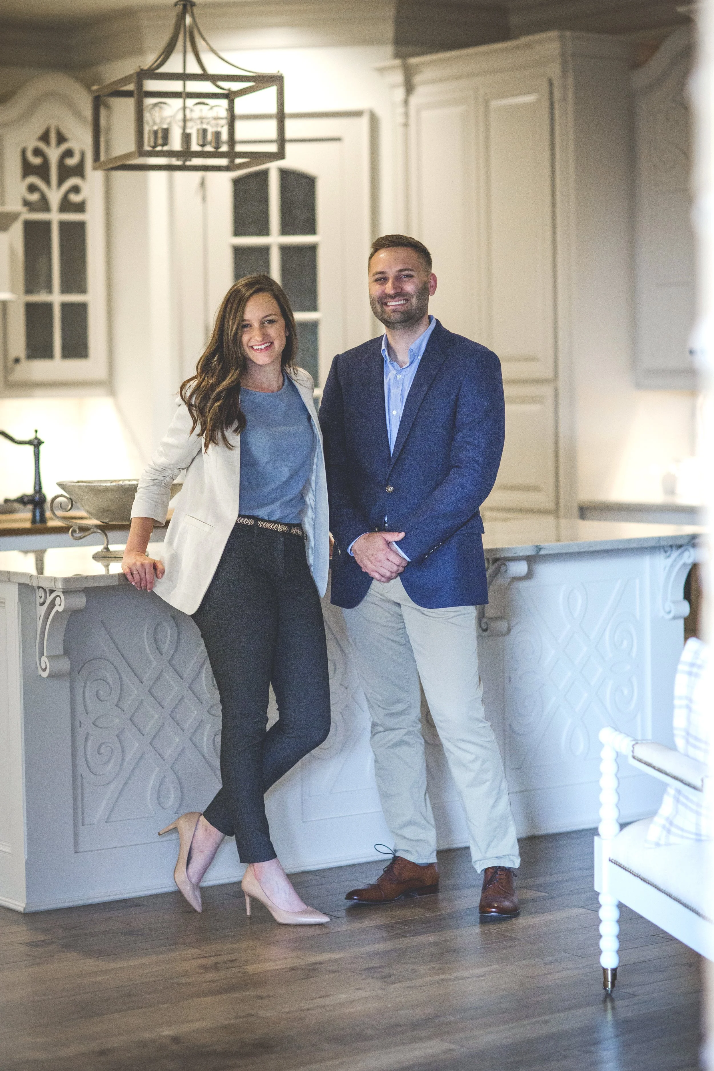 A man and woman standing in a modern kitchen, smiling, with the woman resting her hand on the kitchen counter.