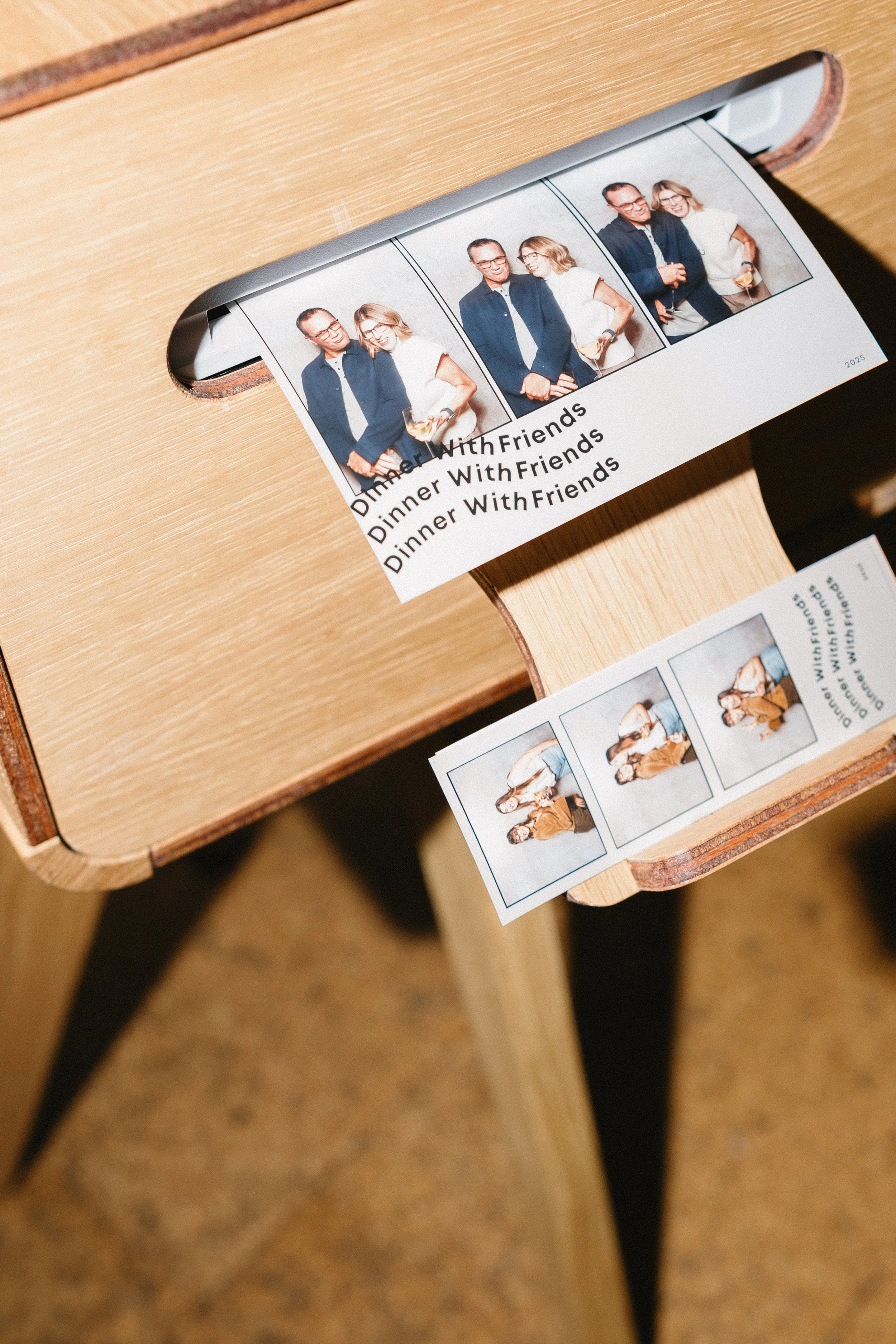 Photo booth photo strip with three pictures of two women sitting together, wearing casual clothes, and smiling. Printed on paper labeled "Dinner With Friends."