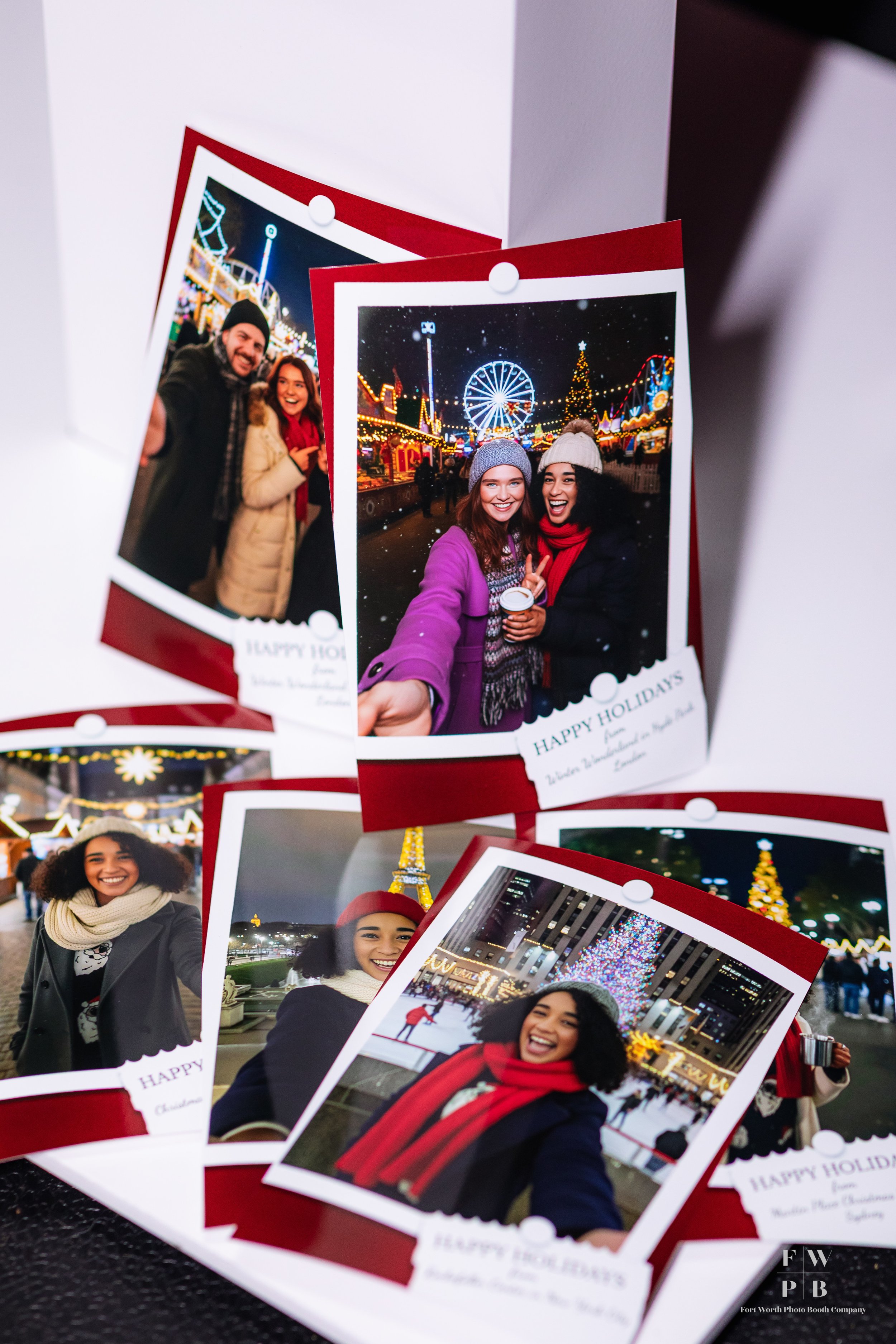 A display of several printed holiday photo cards showing people at a festive amusement park at night, decorated with bright lights, Ferris wheel, holiday trees, and Christmas ornaments.