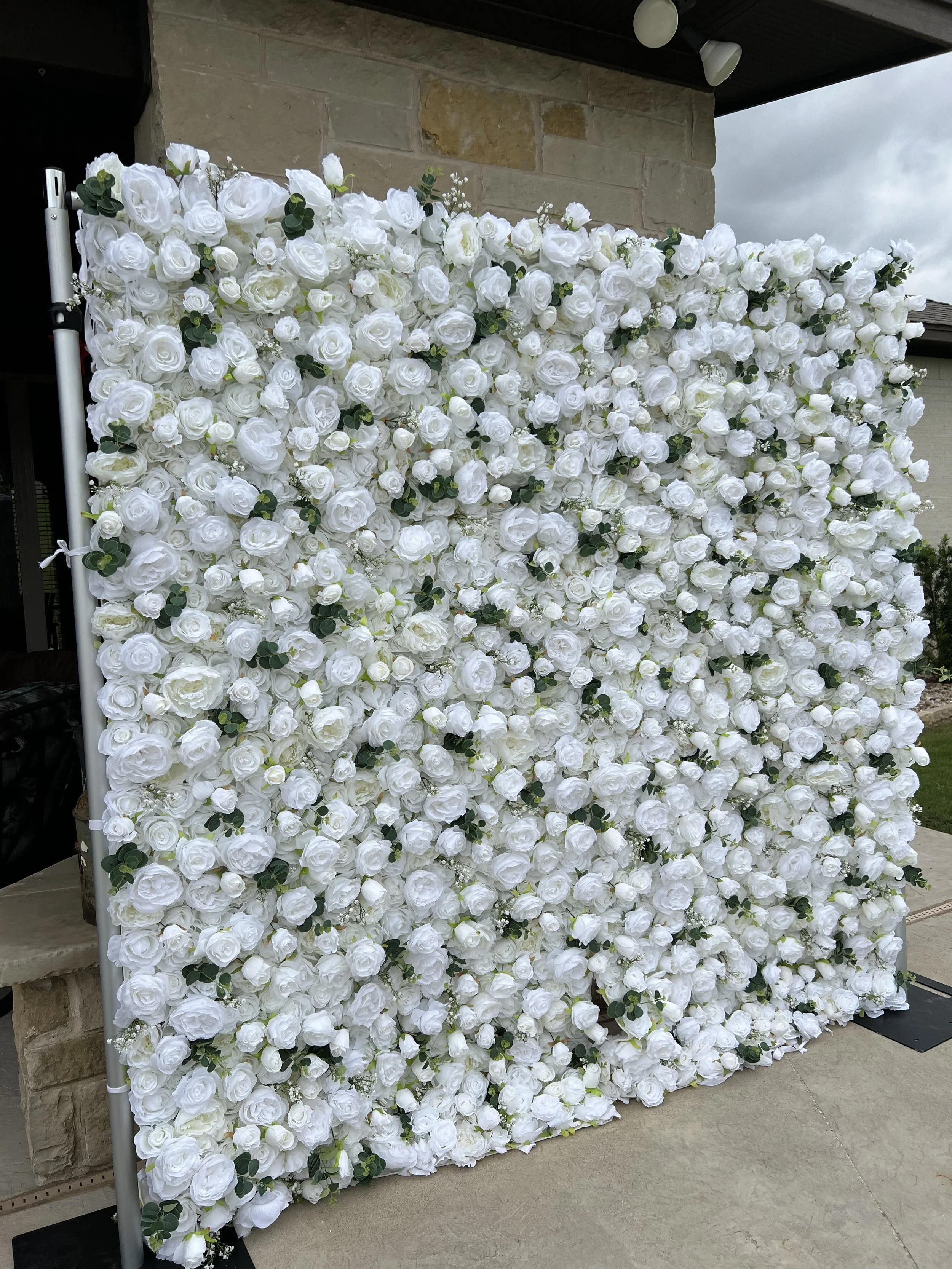 A large floral backdrop made of white roses and greenery, set up outdoors on a patio area.