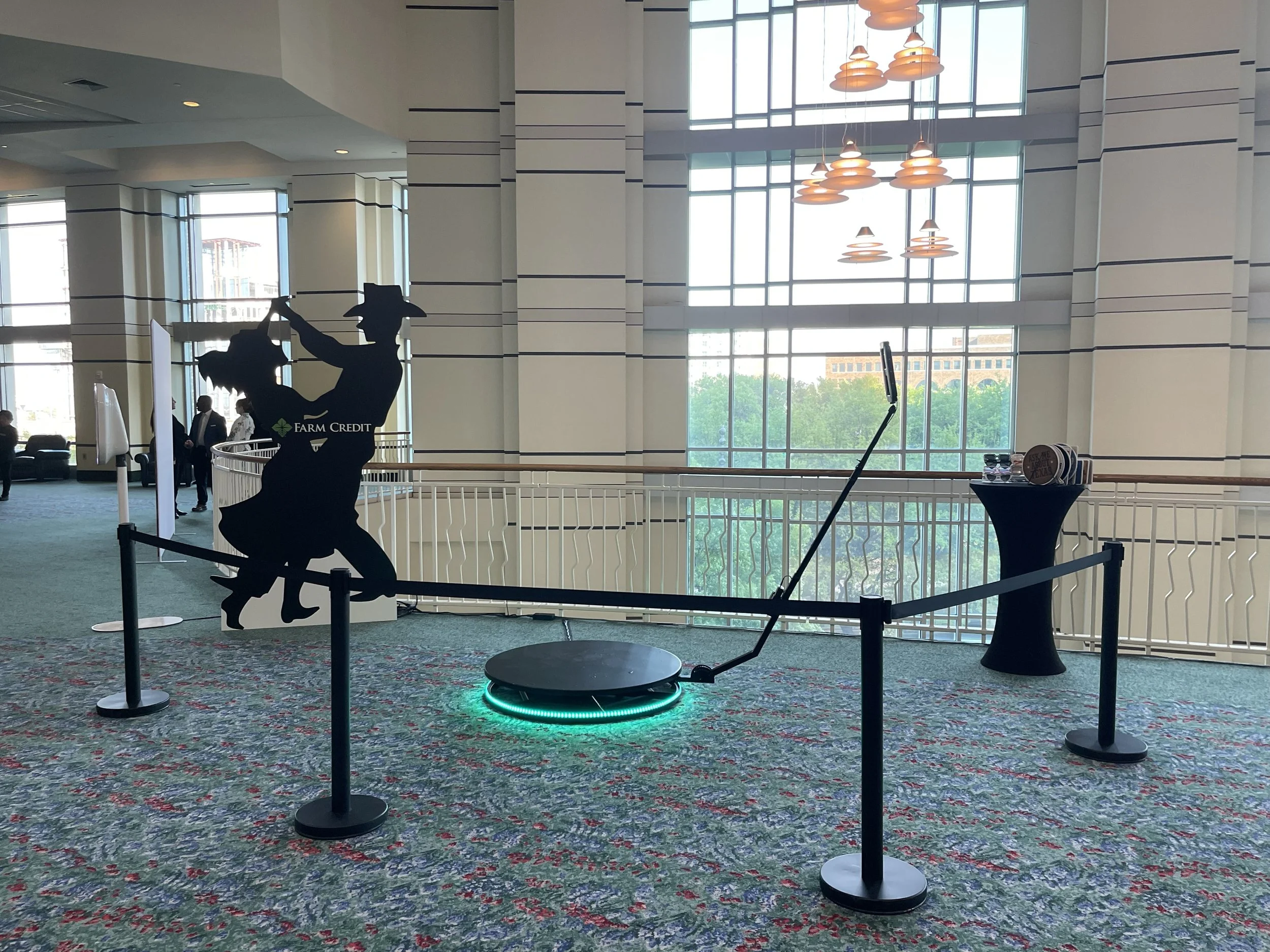 Silhouette of a golfer in a swing pose, with a farm credit logo on the figure, displayed as a cutout inside a roped-off area in a spacious, well-lit lobby with large windows and hanging ceiling lights.
