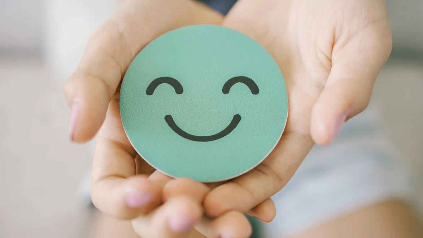 Person holding a round pastel green item with a happy smiling face drawn on it.