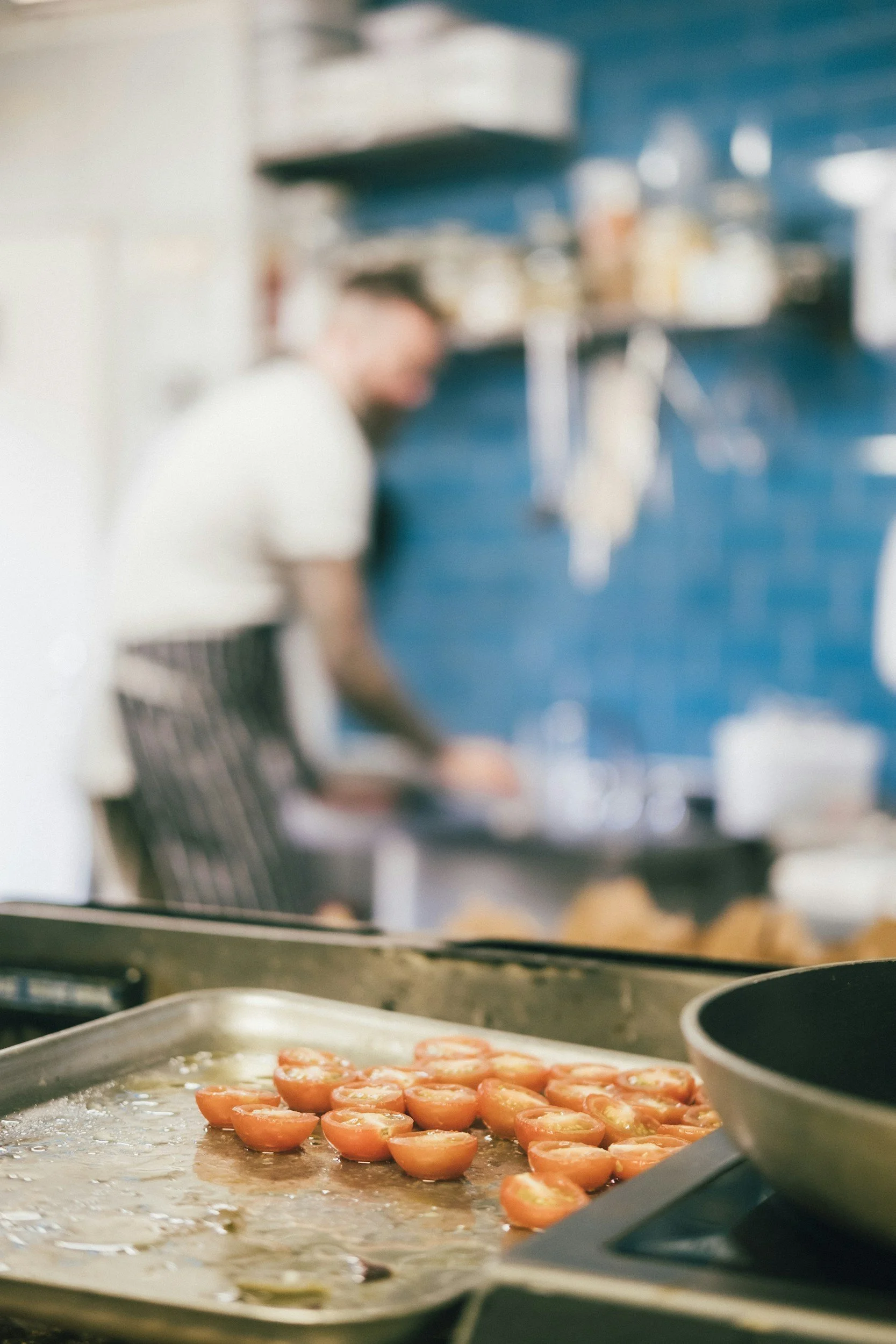 Cherry tomatoes sliced in half on a baking sheet in a kitchen.