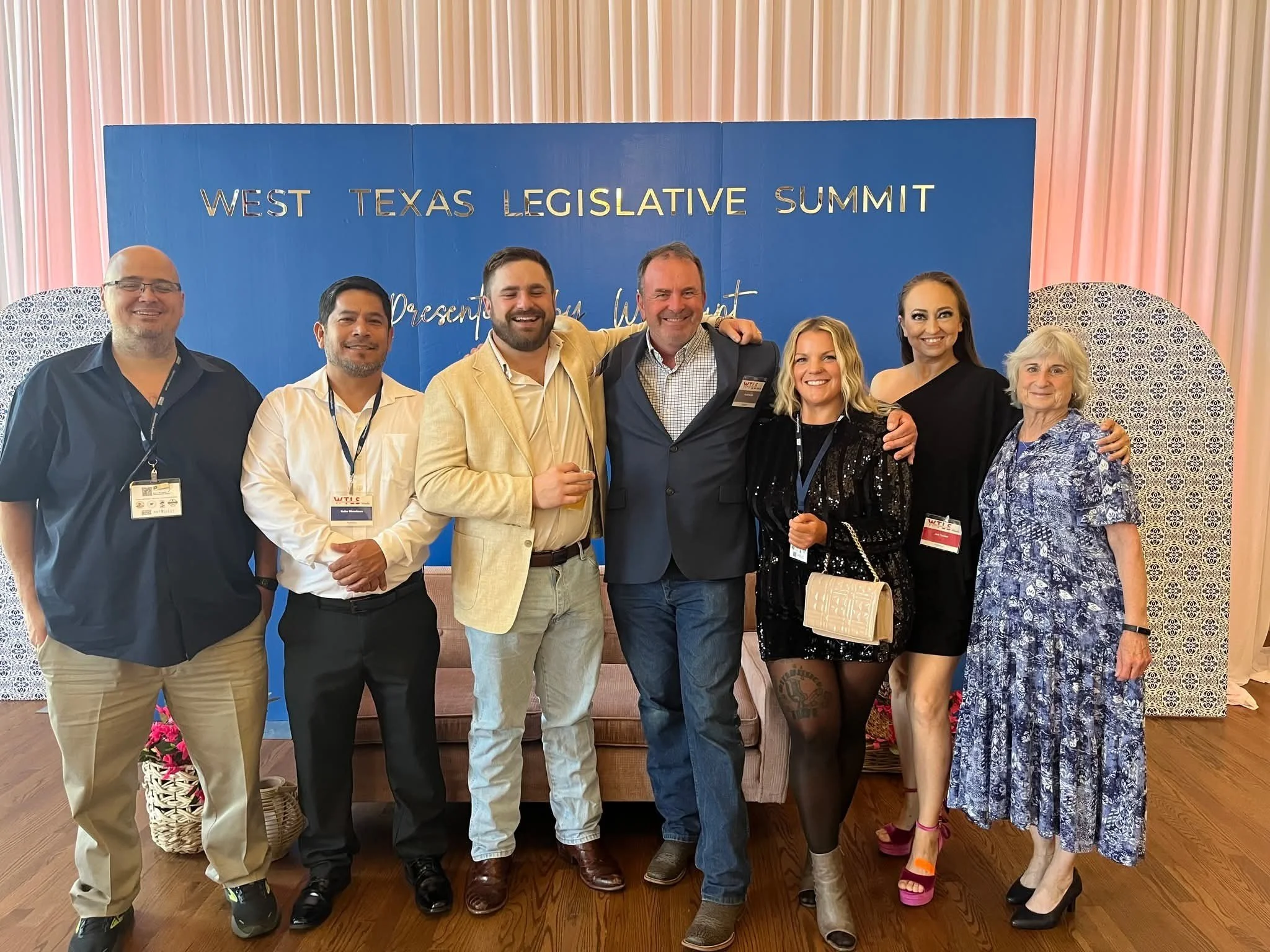 Group of eight people smiling and posing at the West Texas Legislative Summit, standing in front of a blue backdrop with event details.