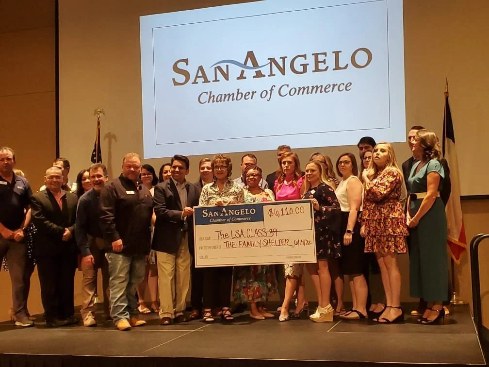 Group of people standing on stage holding a large check at a San Angelo Chamber of Commerce event.