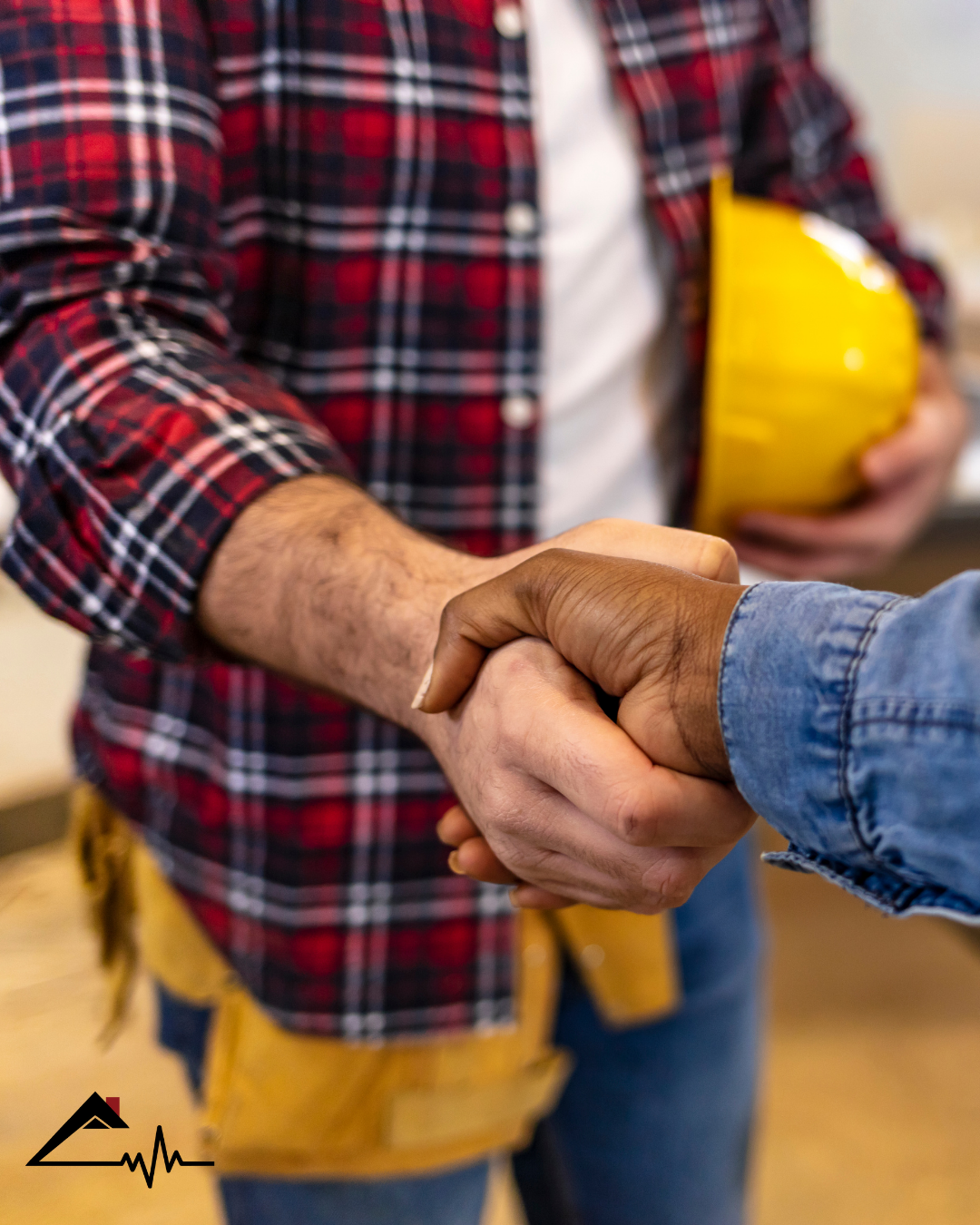 Two people shaking hands, one holding a yellow hard hat, in an indoor work environment.