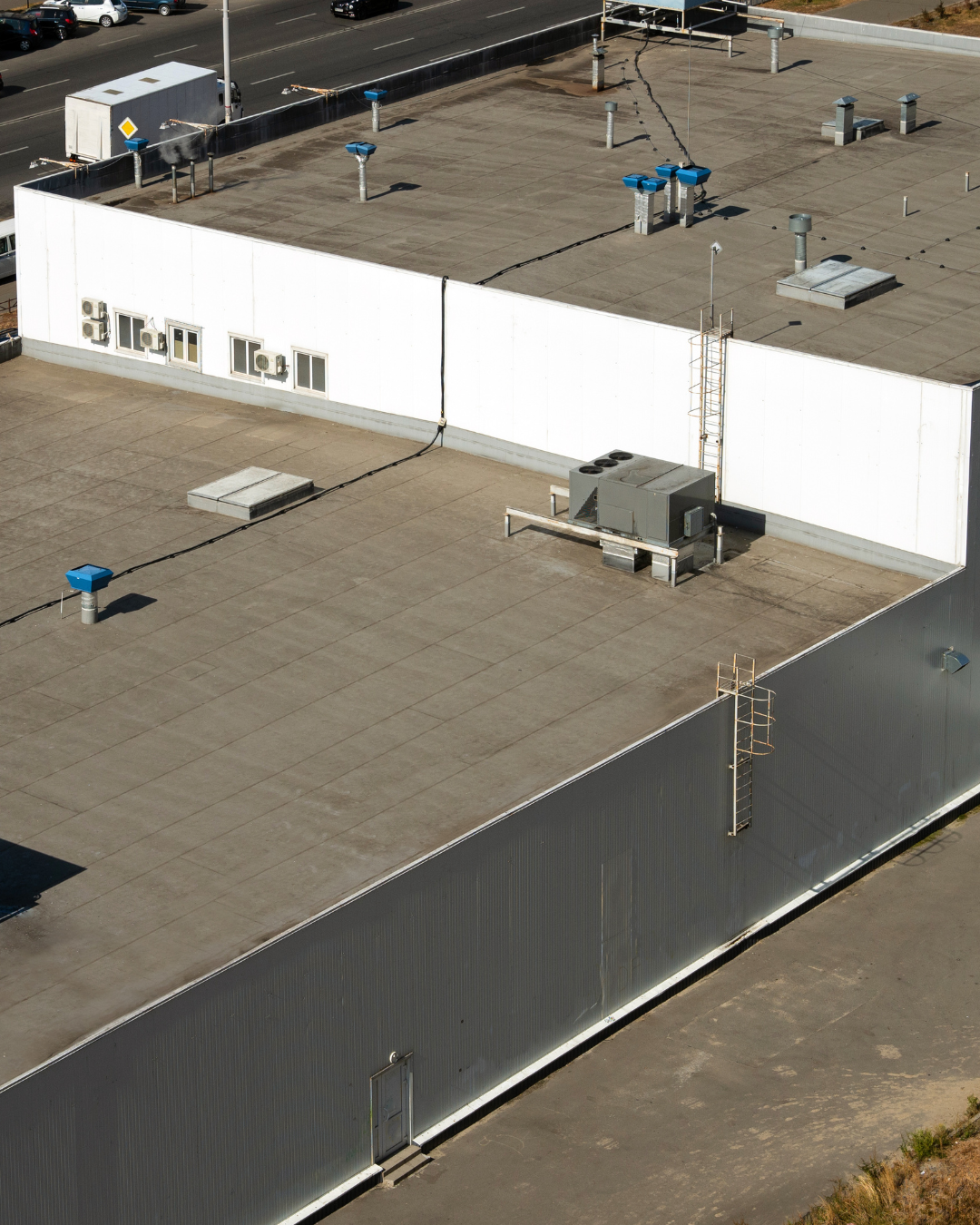 Aerial view of rooftops on commercial buildings showing ventilation units, air conditioning systems, utility vents, and a roof ladder.