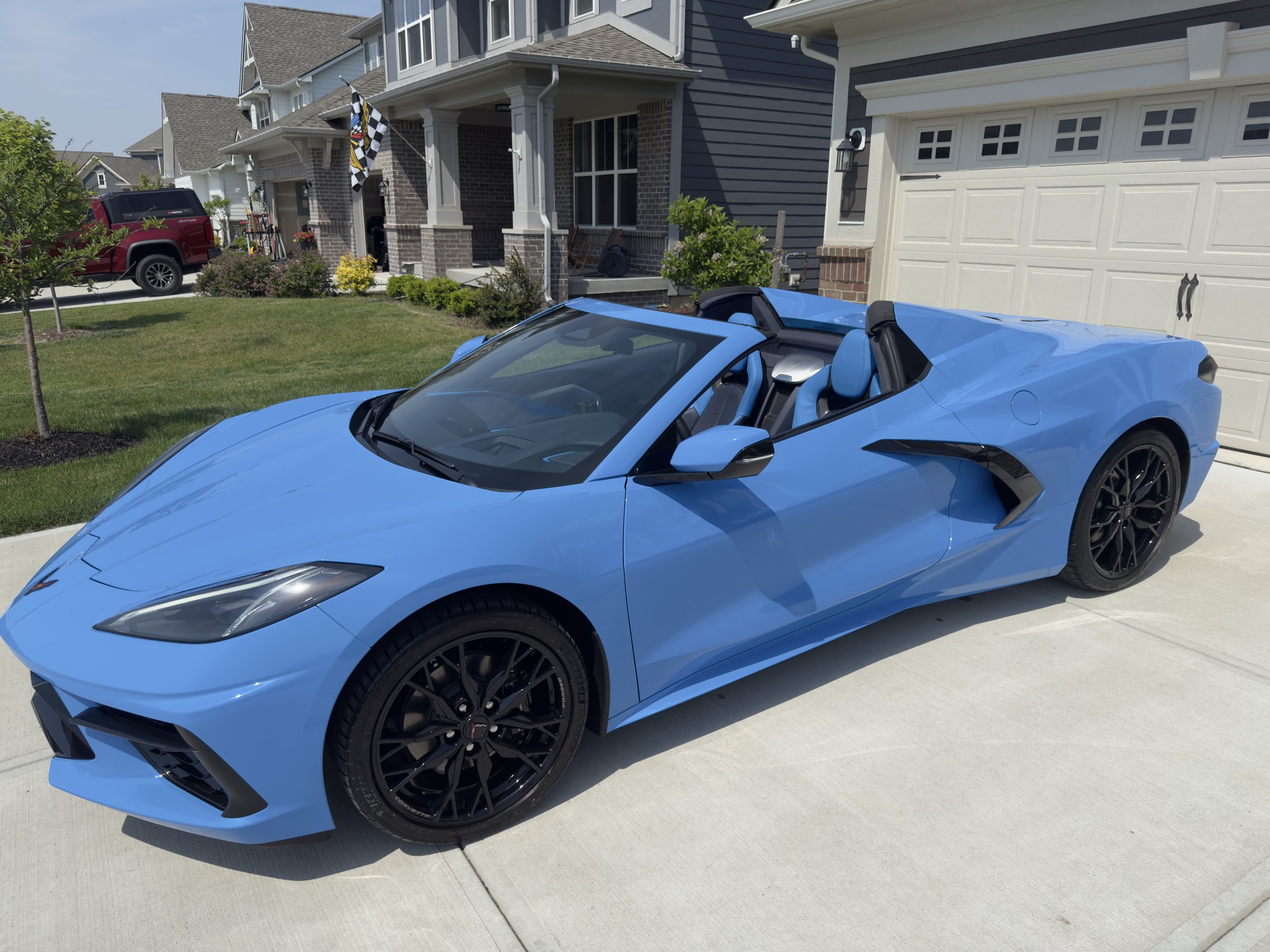 A bright blue convertible sports car parked in a driveway in front of a suburban house with a closed garage door.