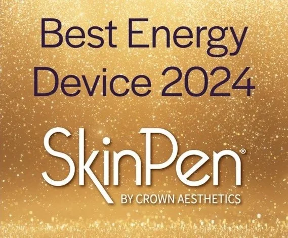 A modern wooden house in a grassy field near a lake with mountains in the background during dawn or dusk.