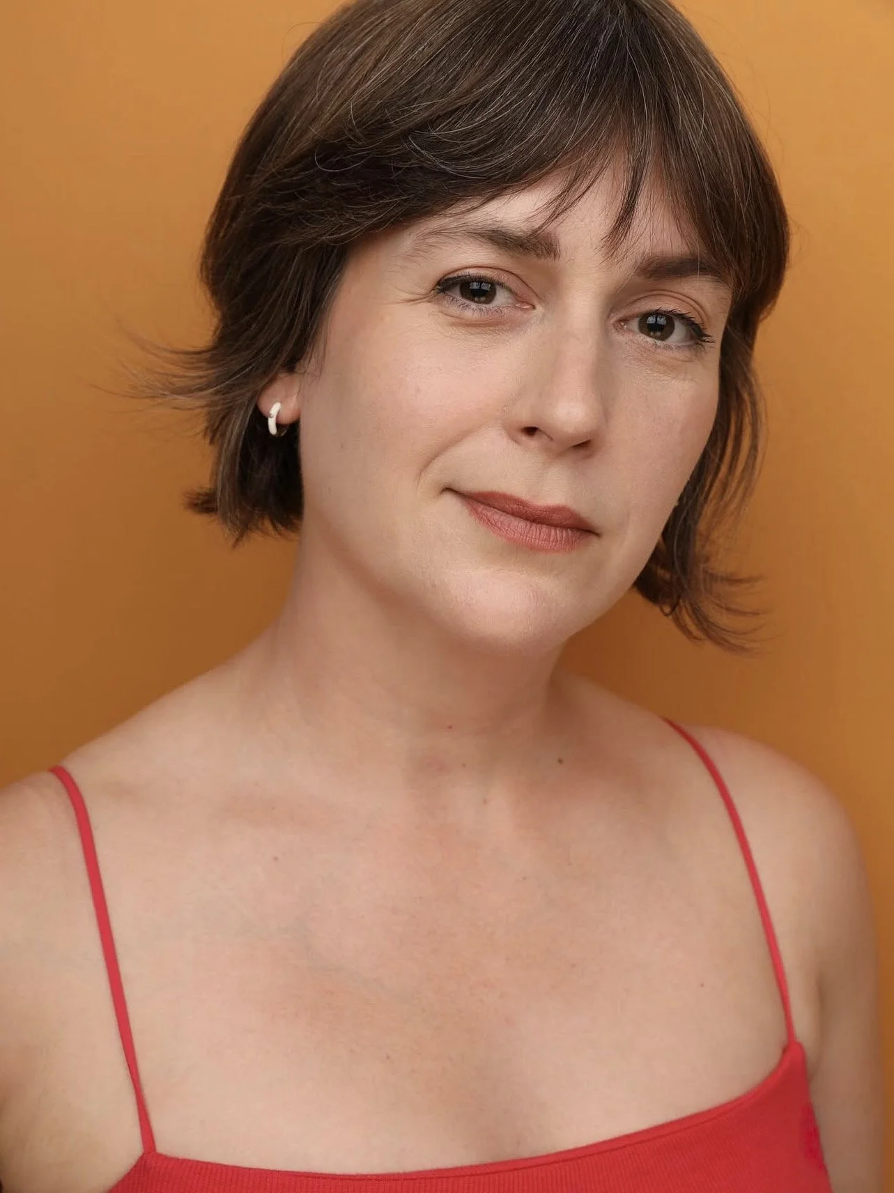 A dark-haired woman in a red tank top smirks at the camera