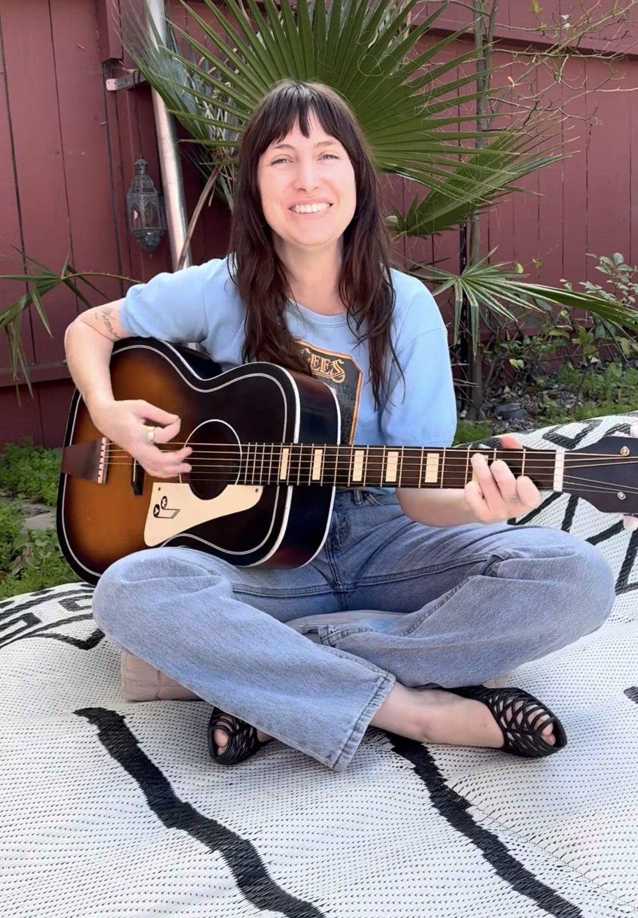 A dark-haired woman holds a guitar and smiles