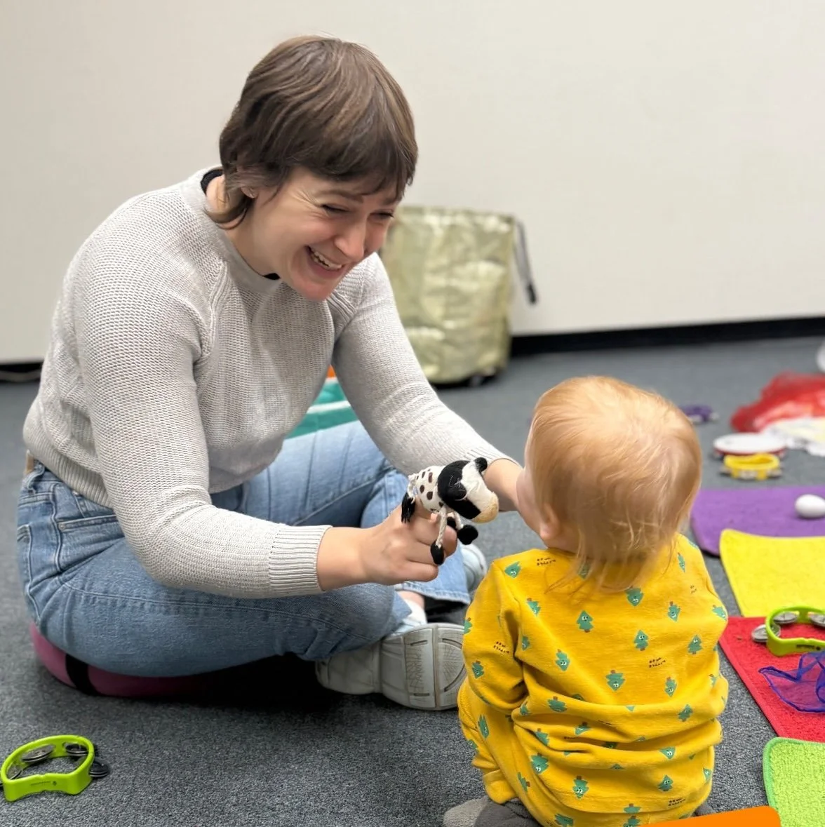 A smiling woman with a short haircut holds a small puppet over a young child