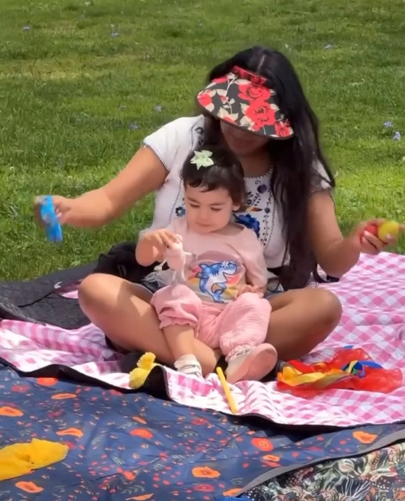 A mother in a colorful hat dances with toys while her young daughter sits on her lap