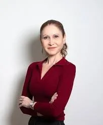 Photo of Natalia Pasternak, a woman with brown hair tied back, wearing a burgundy long-sleeve top, standing against a plain light background with her arms crossed and smiling.
