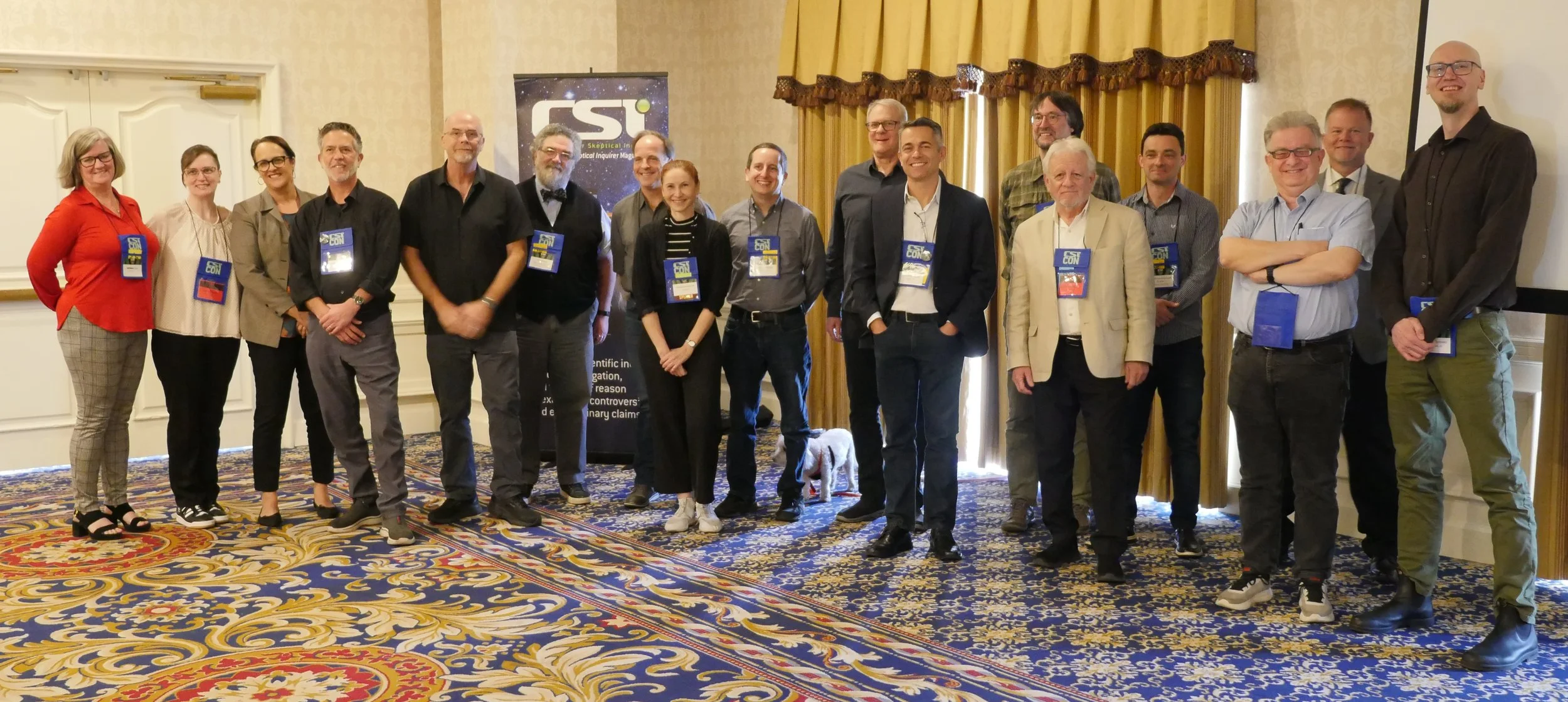 Attendees of LiliCon 2024 standing in a conference room, wearing nametags, with a science-related poster and yellow curtains in the background.